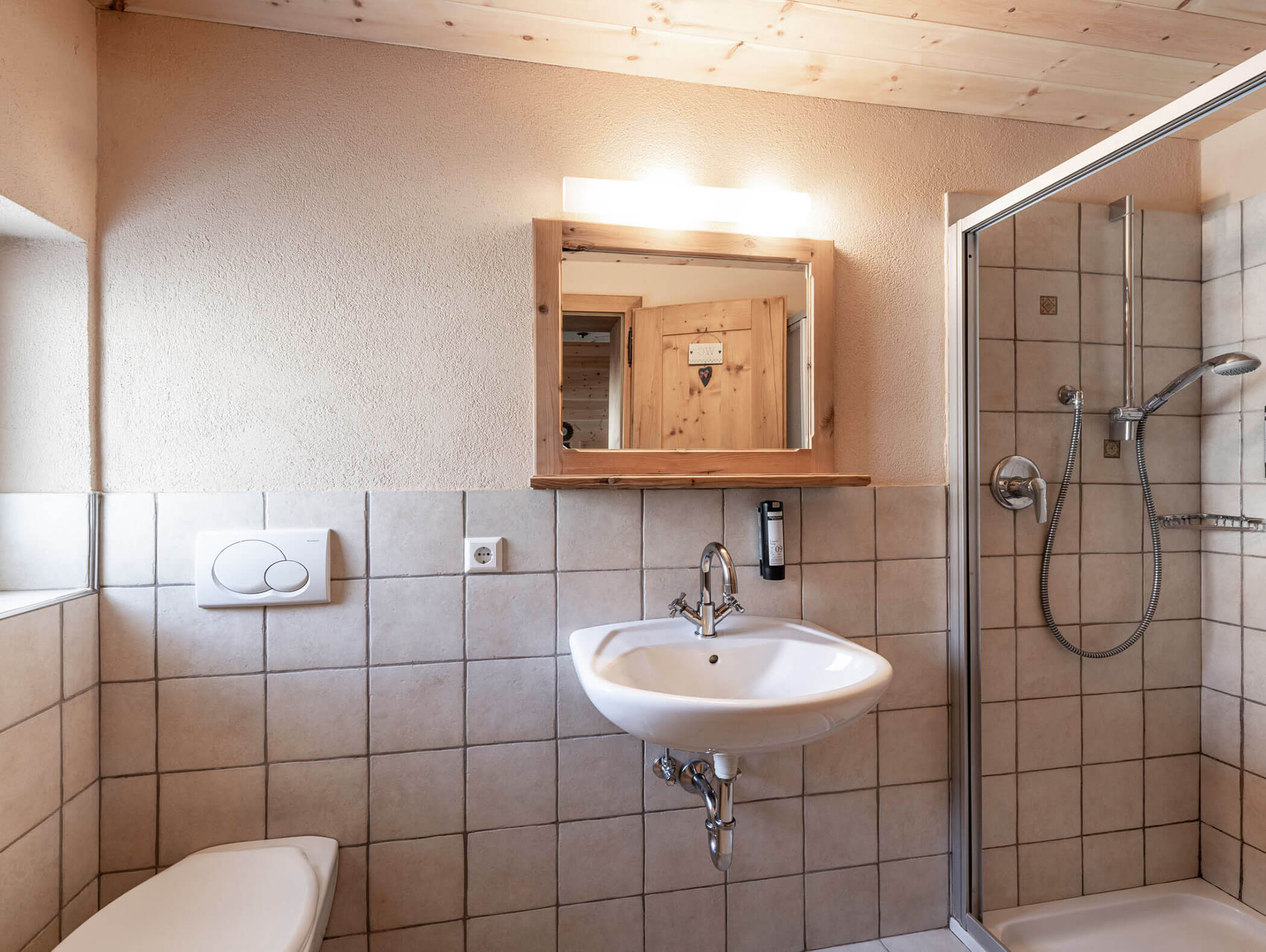Modernes Badezimmer mit Waschbecken, Spiegel, wandmontierter Toilette und Glasdusche mit Handbrause. - Maurlechnhof
