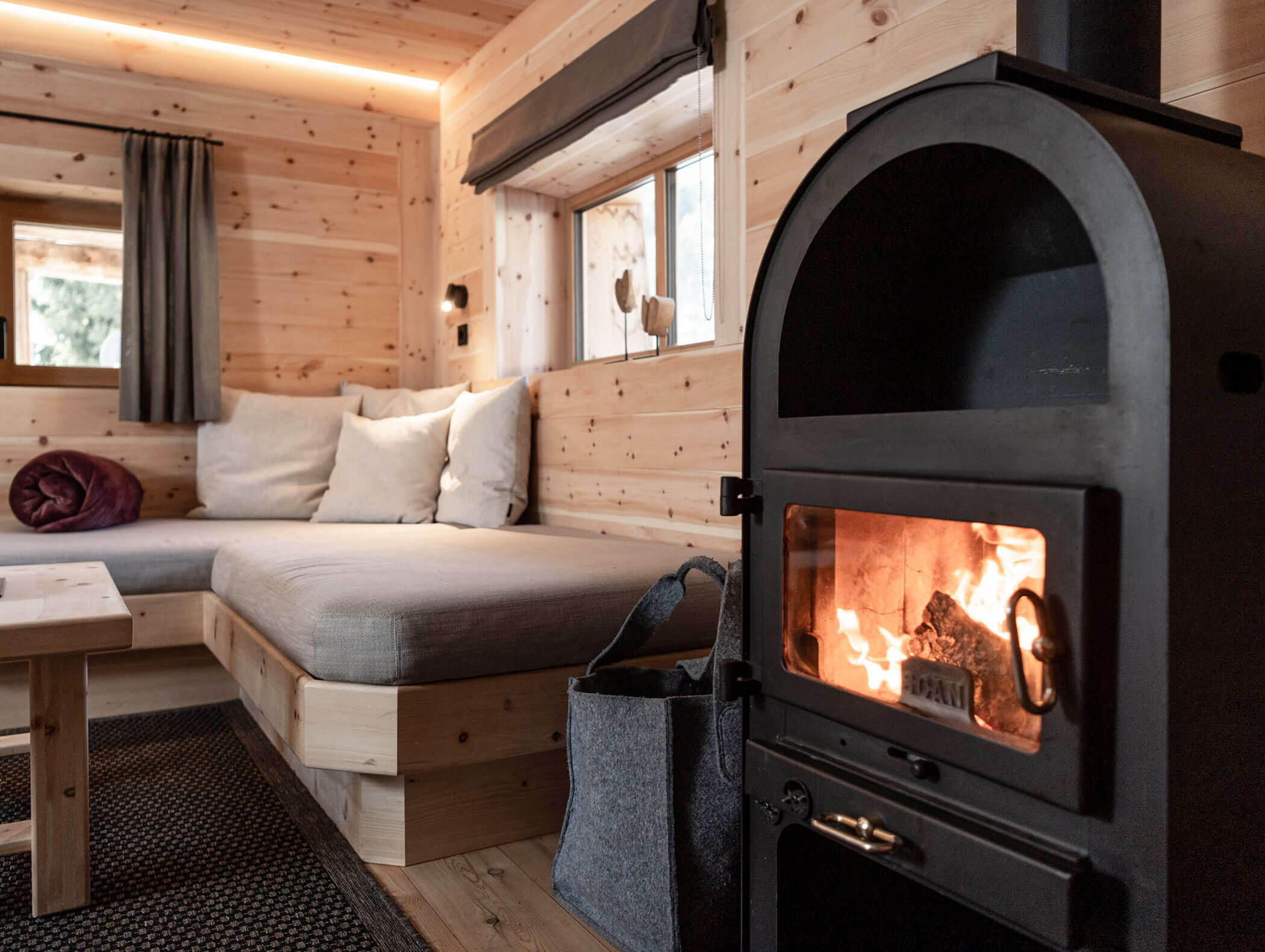 Gemütliche Holzhütte mit einem beleuchteten Kamin, einer gepolsterten Bank, Fenstern und sanfter Beleuchtung. - Maurlechnhof