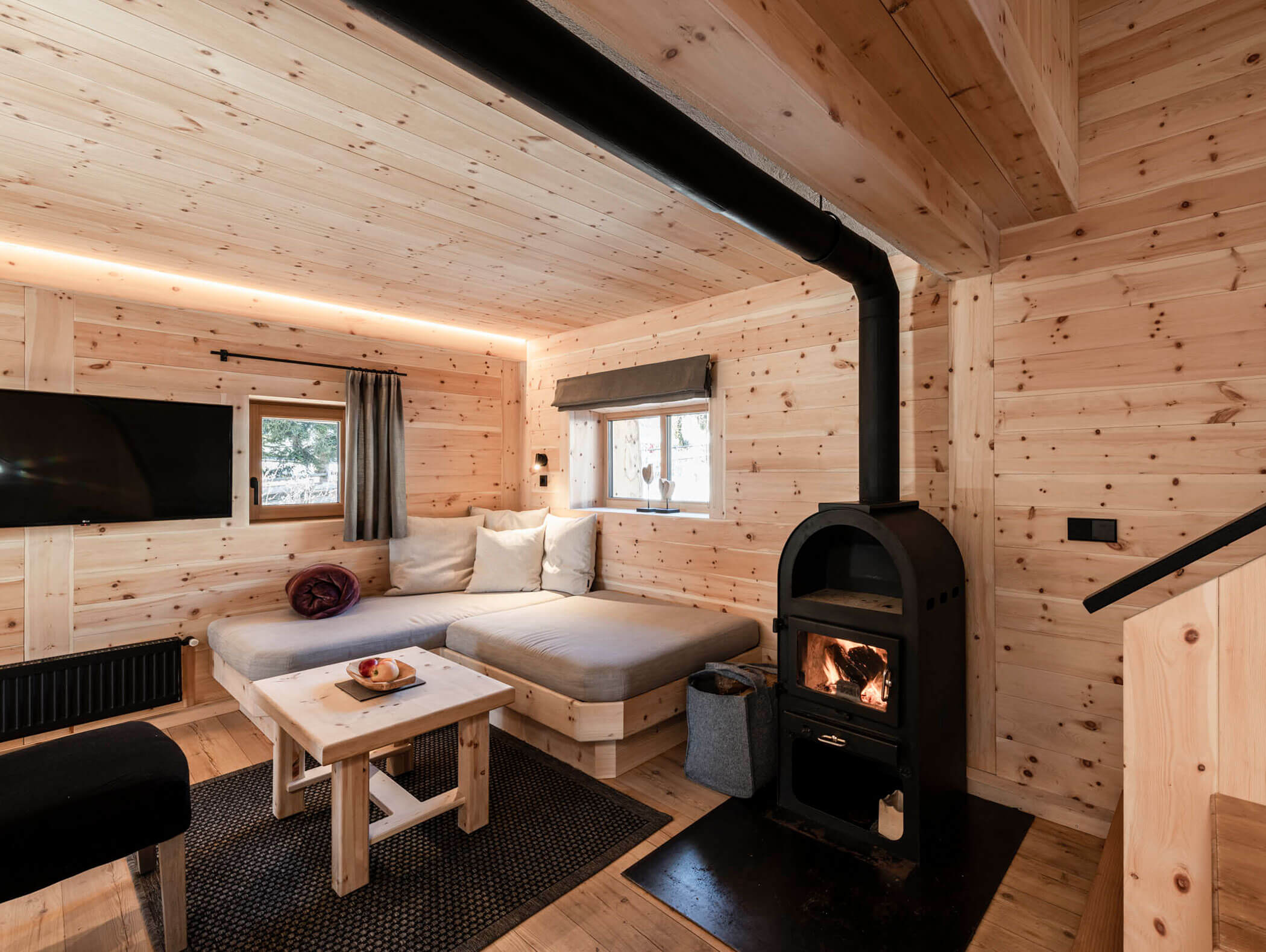 Gemütliche Holzhütte mit Holzofen, grauem Sofa, Couchtisch und großen Fenstern. - Maurlechnhof