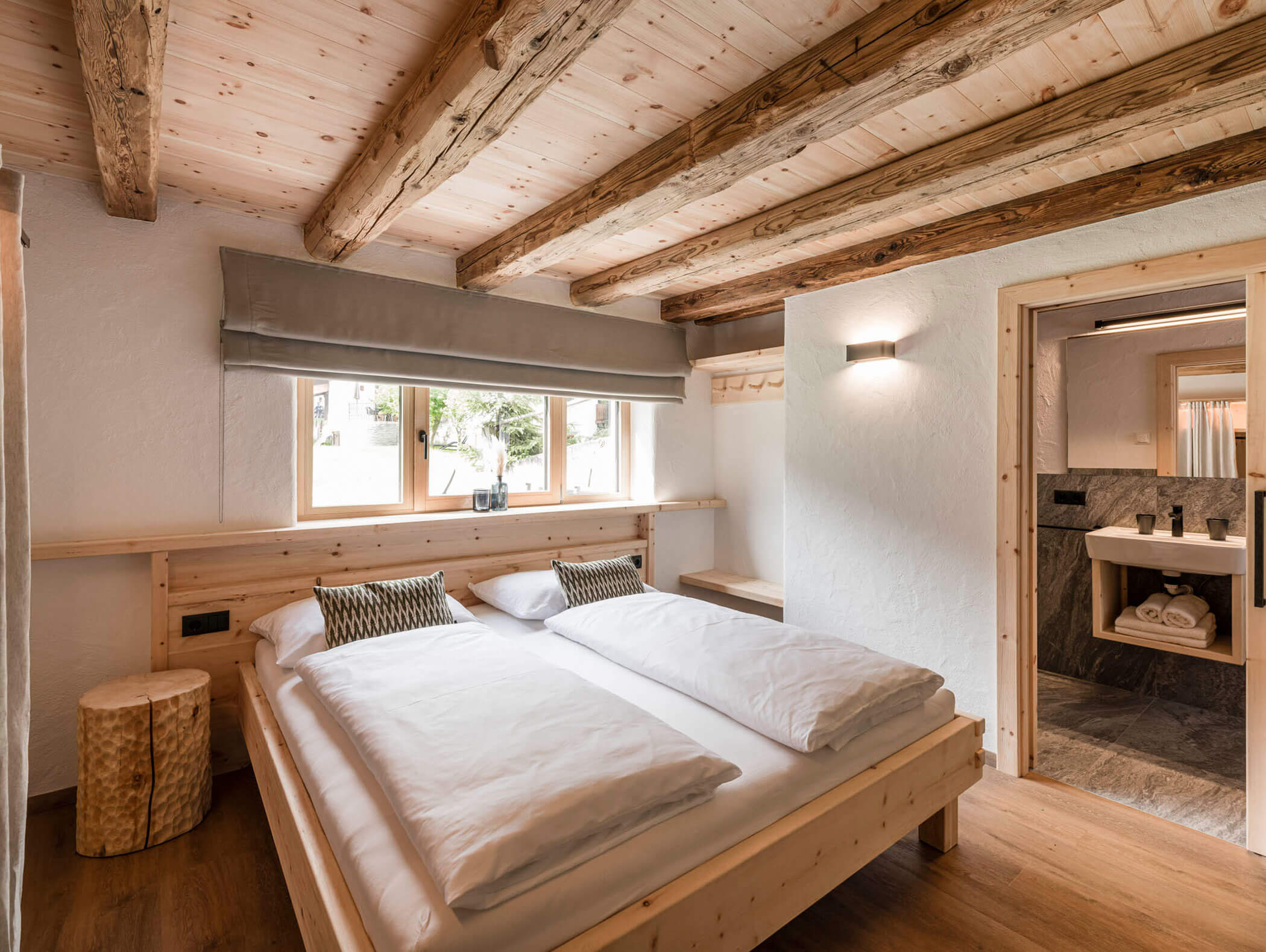 Gemütliches Schlafzimmer mit Holzbalken, Doppelbett, großen Fenstern und Blick in ein modernes Bad. - Maurlechnhof