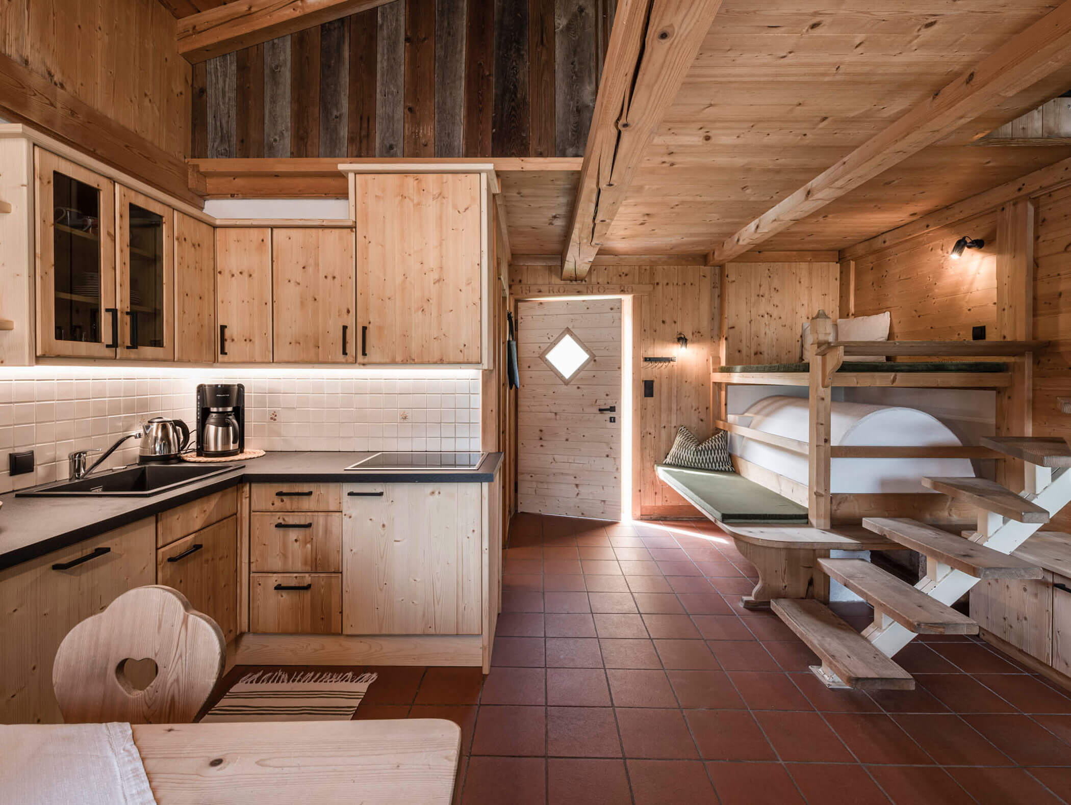 Gemütliche Holzhütte mit Kochnische, Etagenbetten, Esstisch und Tageslicht von der Tür aus. - Maurlechnhof