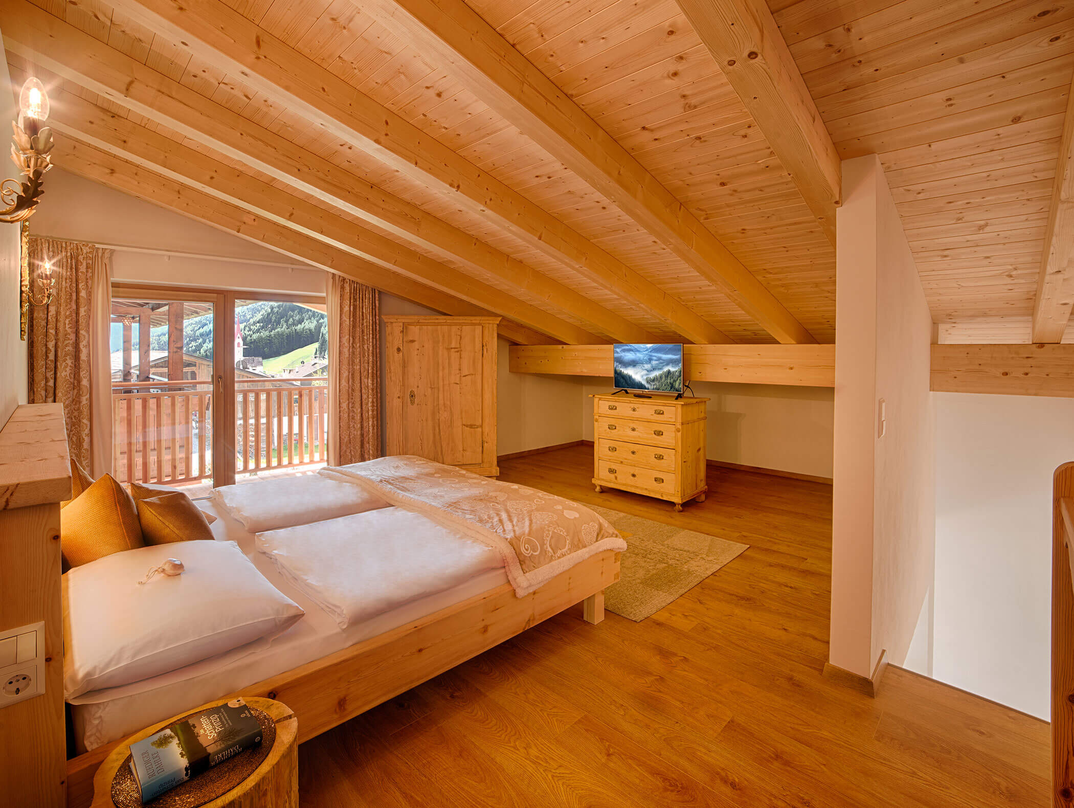Gemütliches Schlafzimmer im Dachgeschoss mit Holzdecke, Doppelbett, Balkonblick, TV und warmer Beleuchtung. - Maurlechnhof