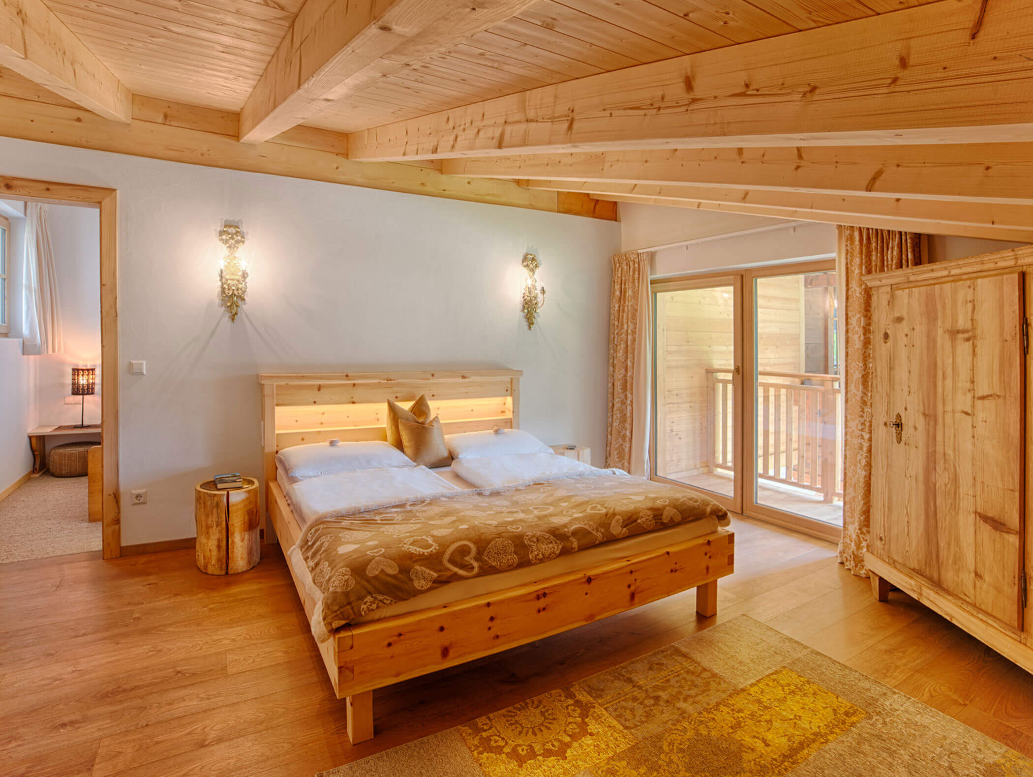 Gemütliches Holzschlafzimmer mit Doppelbett, Kleiderschrank, gedämpfter Beleuchtung und Zugang zum Balkon durch Glastüren. - Maurlechnhof