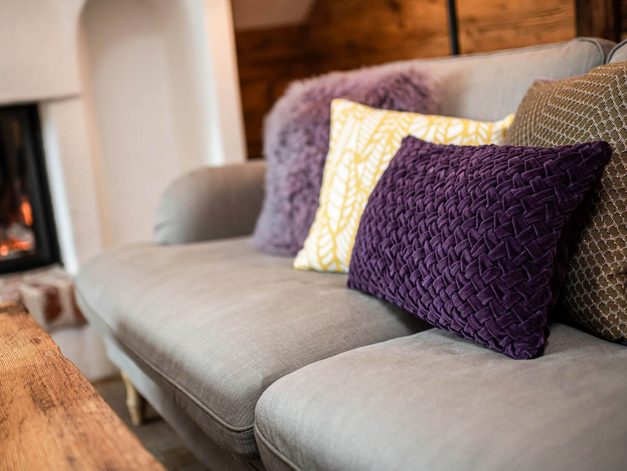 Nahaufnahme eines grauen Sofas mit dekorativen Kissen in Lila, Gelb und Braun neben einem Holztisch. - Maurlechnhof