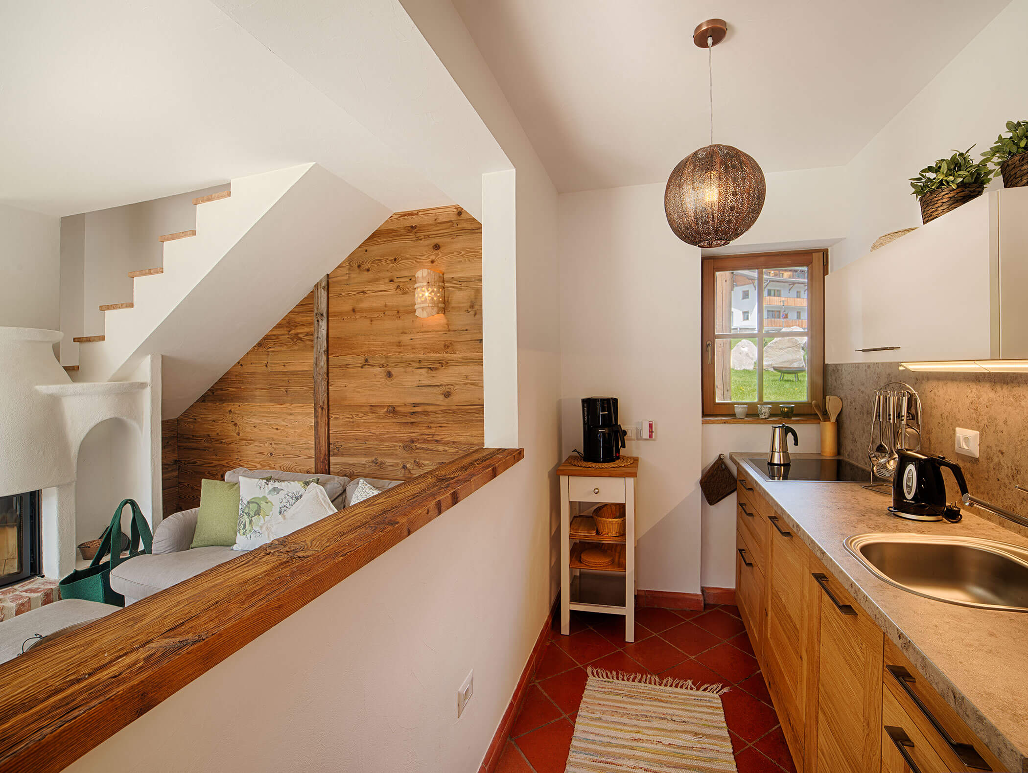 Moderne Küchenzeile mit Holzschränken, ein kleiner Wohnbereich und eine Treppe in einer gemütlichen, hellen Wohnung. - Maurlechnhof