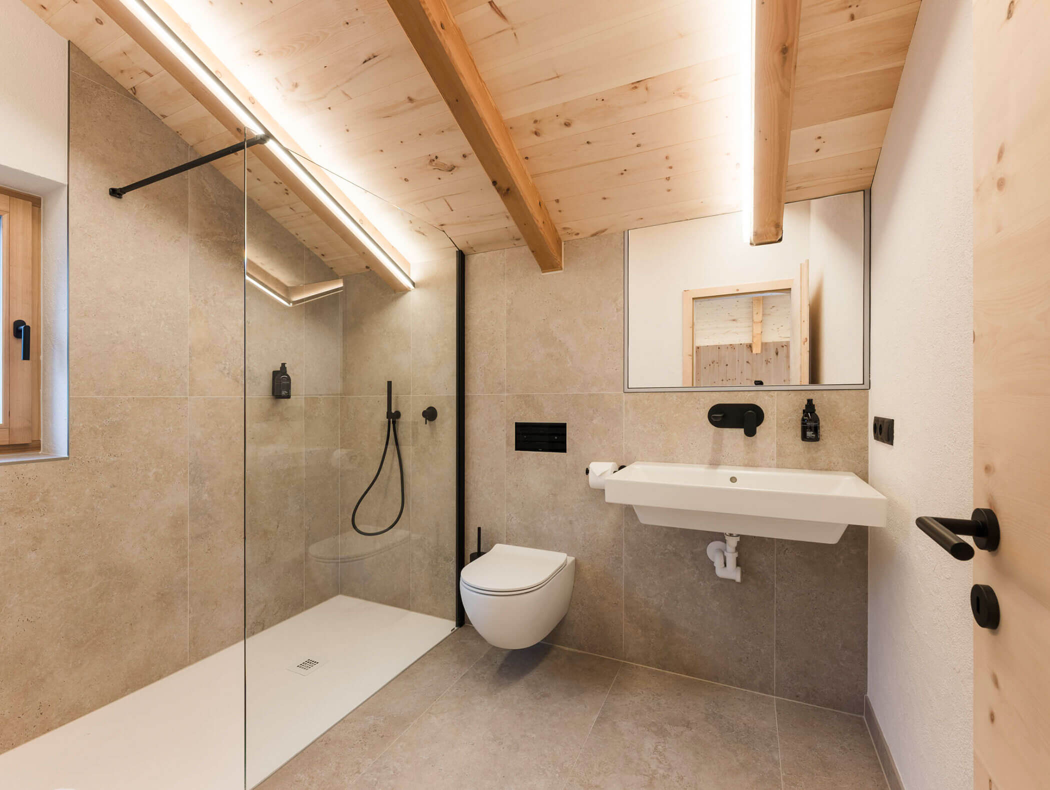 Modernes Badezimmer mit Holzdecke, begehbarer Dusche, wandmontierter Toilette und Waschbecken mit großem Spiegel. - Maurlechnhof