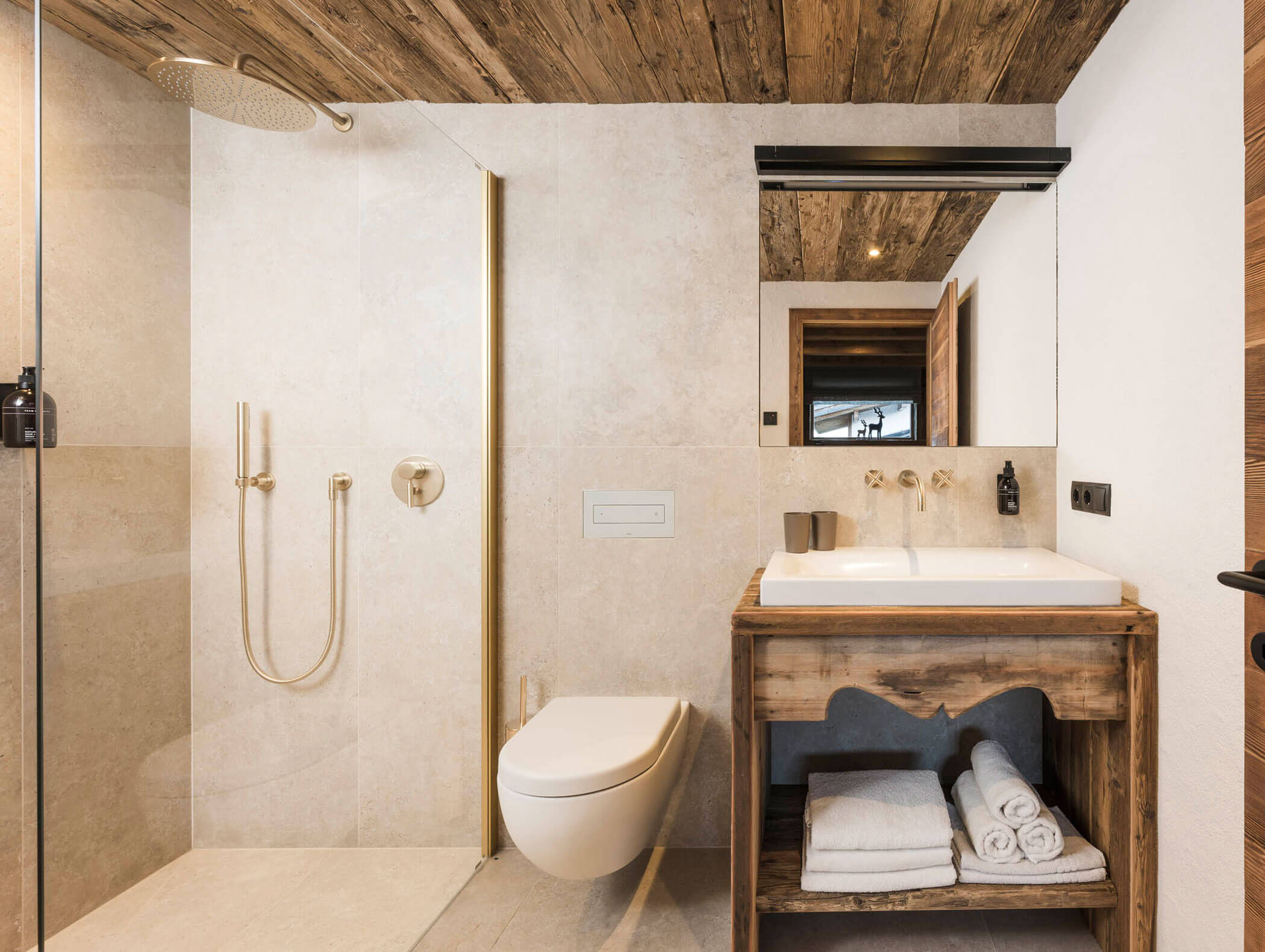 Modernes Badezimmer mit begehbarer Dusche, wandmontierter Toilette, hölzernem Waschbeckenschrank und ordentlich gefalteten Handtüchern. - Maurlechnhof
