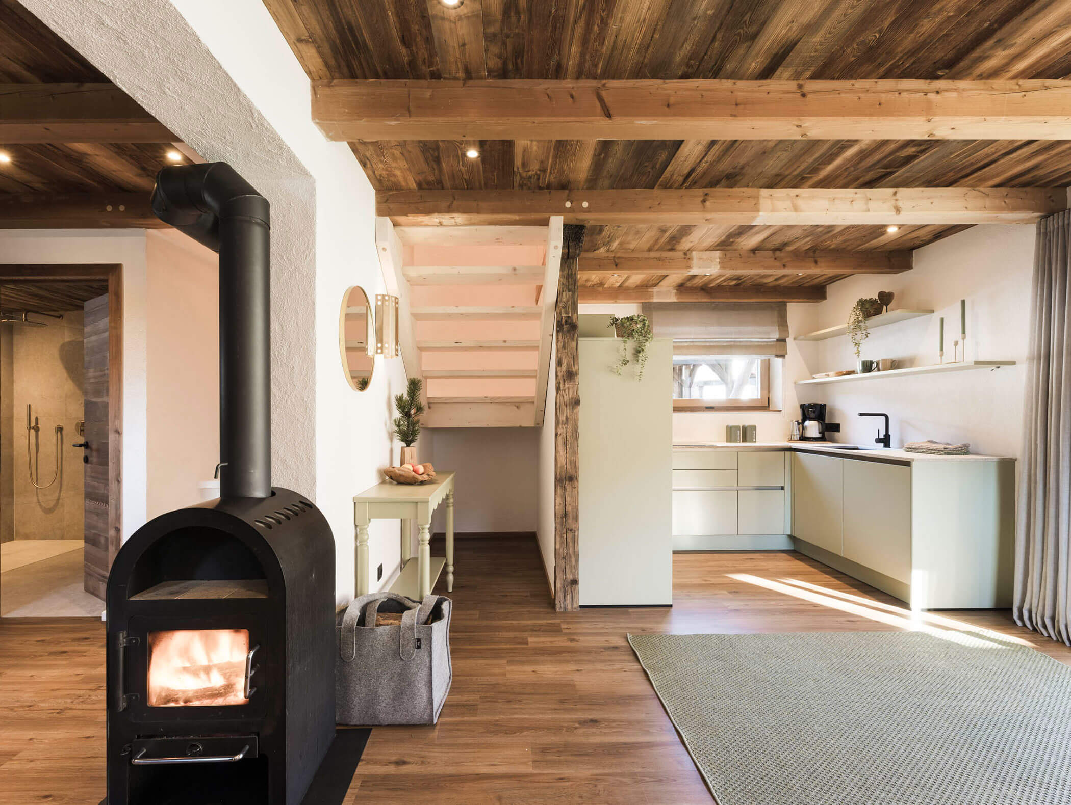 Moderne rustikale Küche und Wohnbereich mit Holzdecke, Holzofen und hellen Schränken. - Maurlechnhof