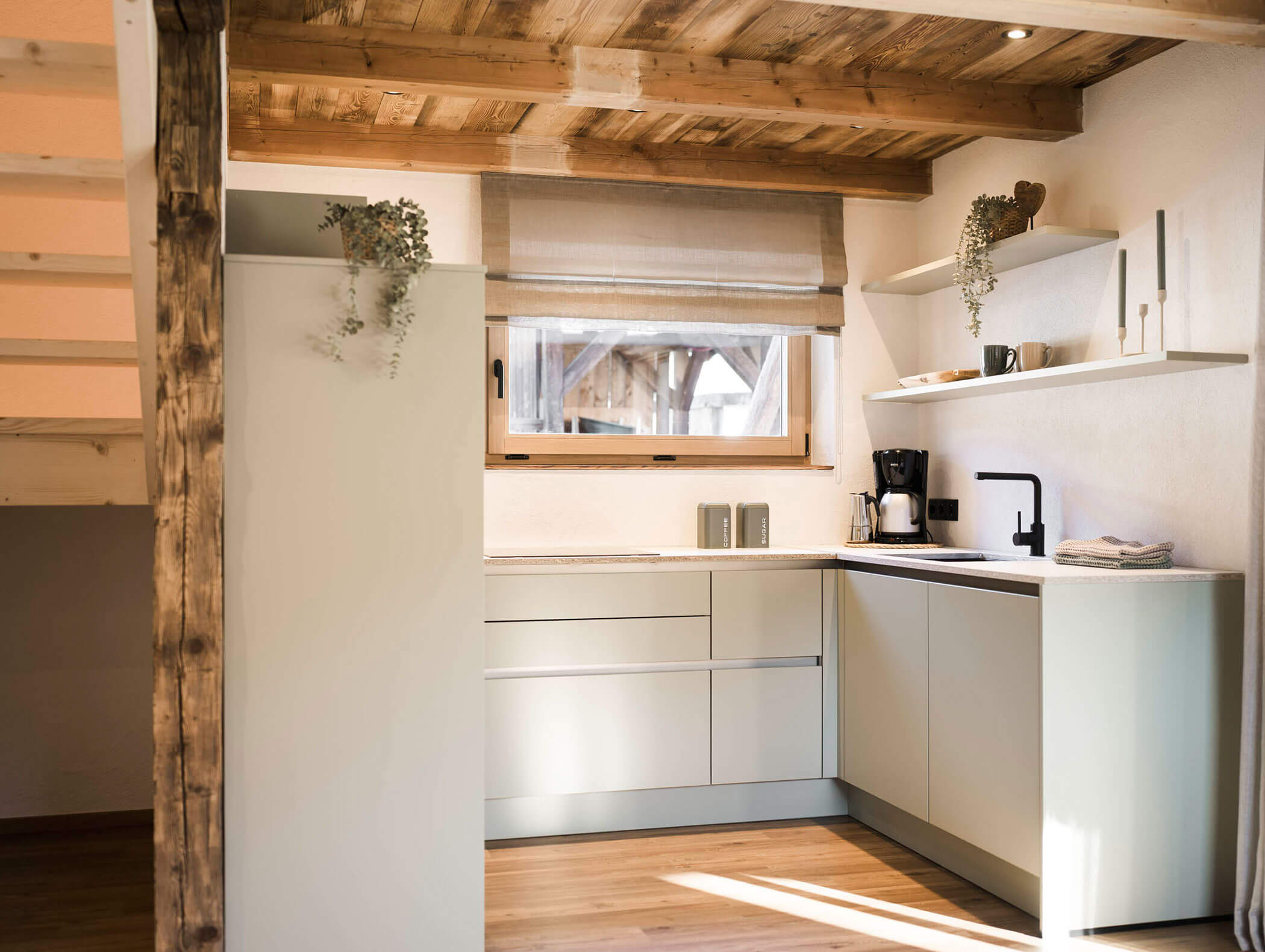 Moderne Küche mit weißen Schränken, Holzdecke, offenen Regalen, Fenster und minimalem Dekor. - Maurlechnhof