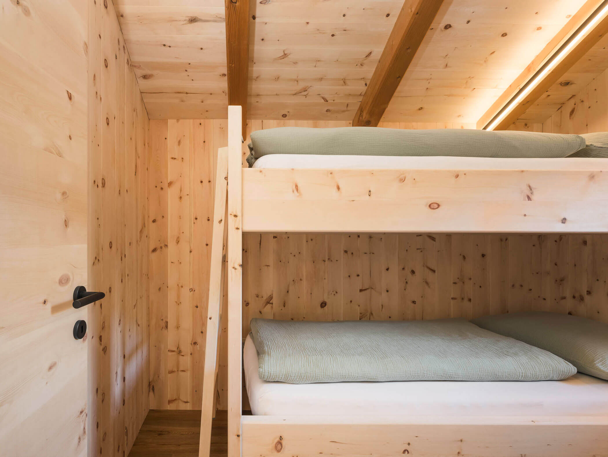Holzgetäfelter Raum mit einem Etagenbett aus Holz, jedes mit einer grünen Decke, neben einer geschlossenen Tür. - Maurlechnhof