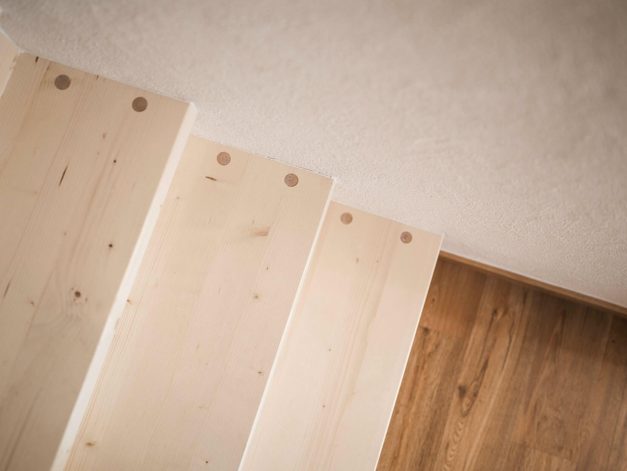 Draufsicht auf drei helle Holztreppen neben einer Wand, die zu einem braunen Holzboden hinunterführen. - Maurlechnhof