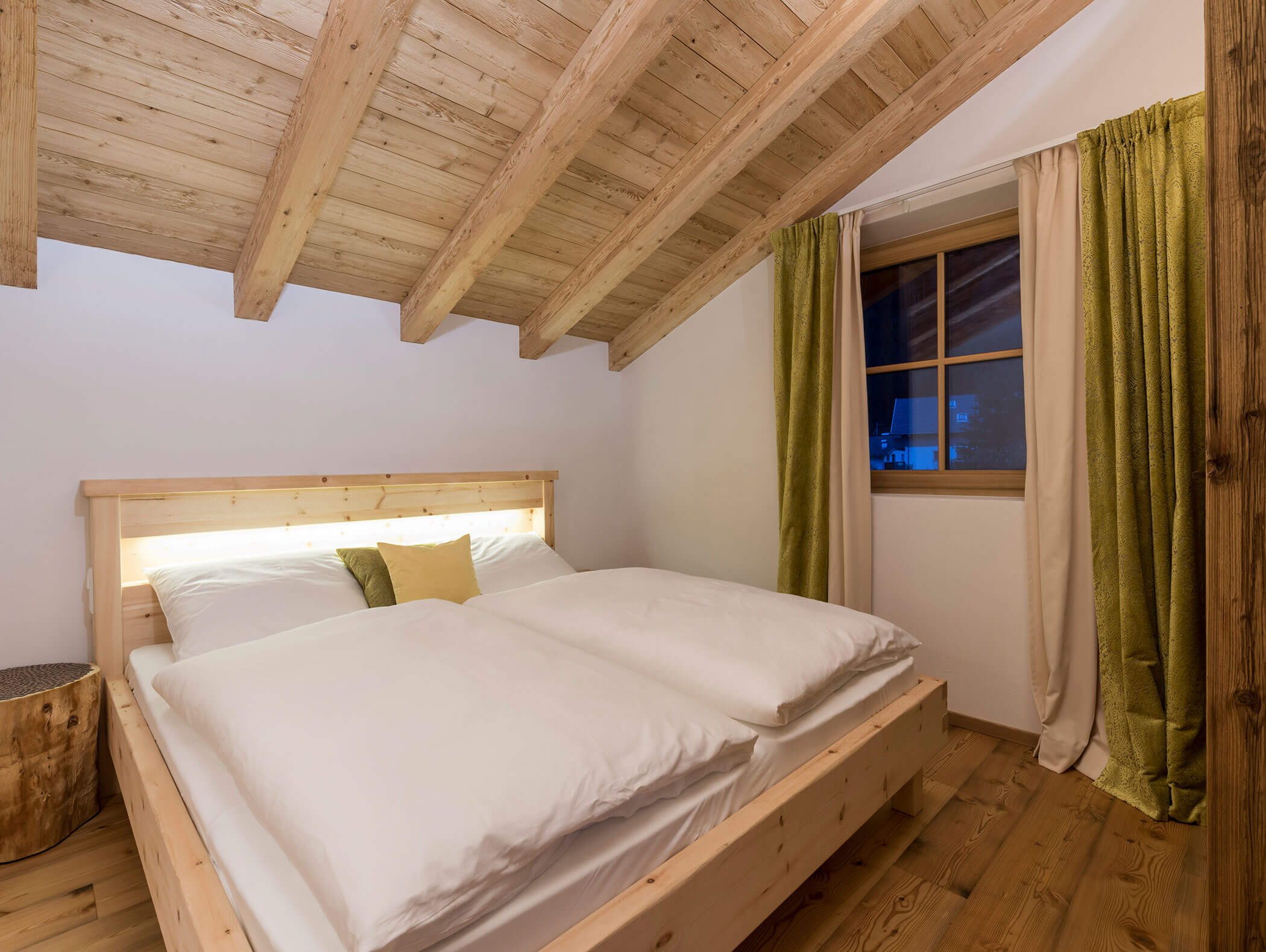 Gemütliches Schlafzimmer im Dachgeschoss mit Holzbalken, einem Doppelbett, grünen Vorhängen und einem Fenster für die Nacht. - Maurlechnhof