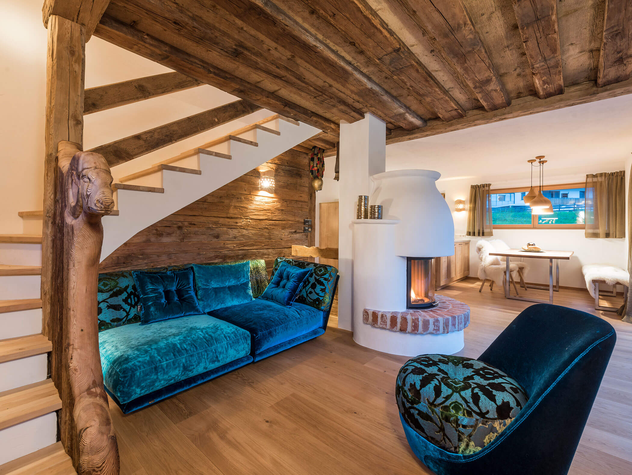 Gemütliches, rustikales Wohnzimmer mit Holzbalken, tealfarbenen Samtmöbeln und einem weißen Kamin in der Nähe des Essbereichs. - Maurlechnhof