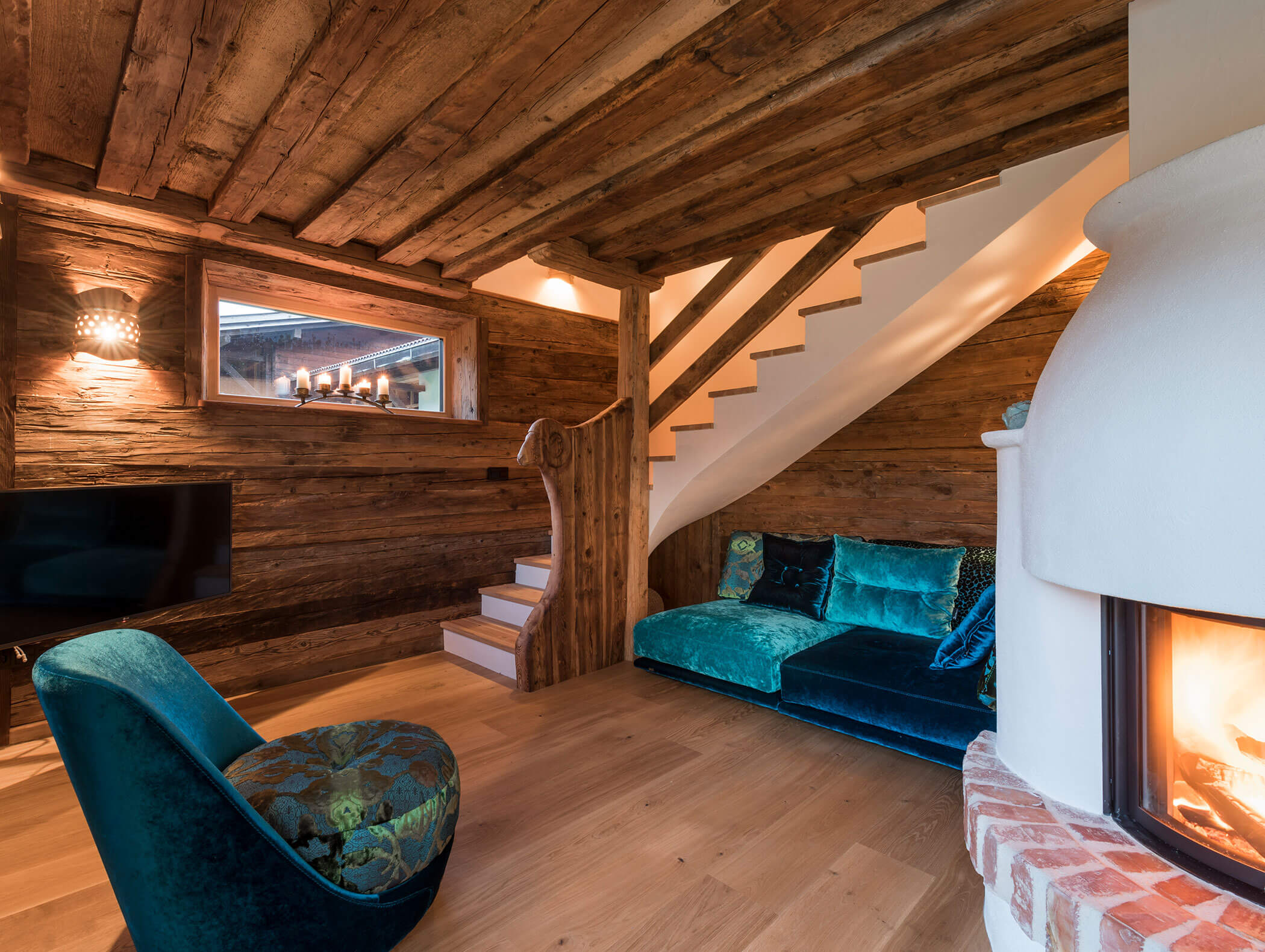 Gemütliches rustikales Wohnzimmer mit Holzwänden, türkisfarbenen Sitzgelegenheiten, Kamin und Treppe mit Holzakzenten. - Maurlechnhof
