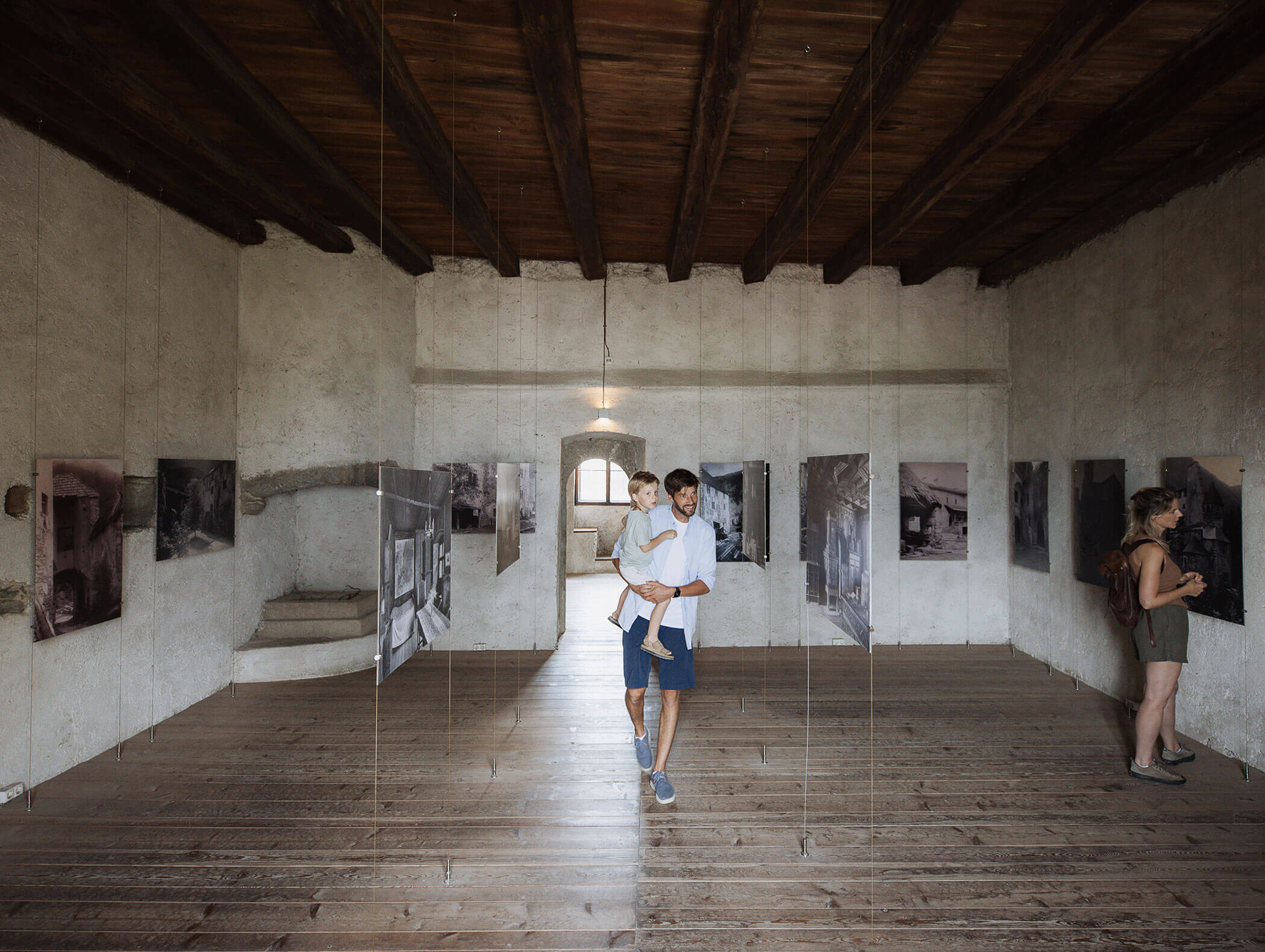 Ein Mann mit einem Kind geht durch eine Kunstgalerie mit Fotos an den Wänden; eine andere Person betrachtet ein Kunstwerk. - Maurlechnhof