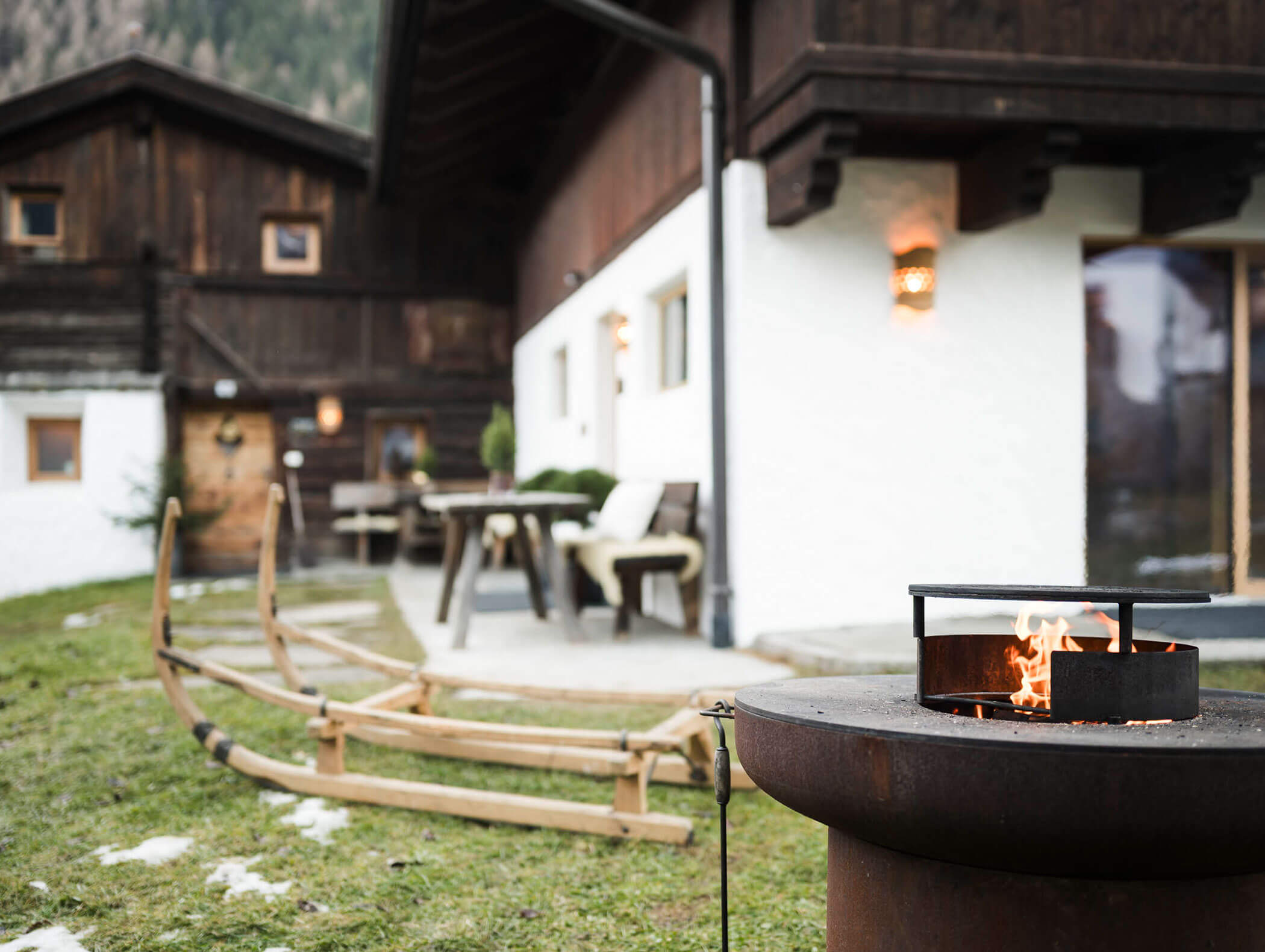 Eine rustikale Hütte mit einer Feuerstelle, einem Holzschlitten und Terrassenmöbeln auf einer Wiese. - Maurlechnhof