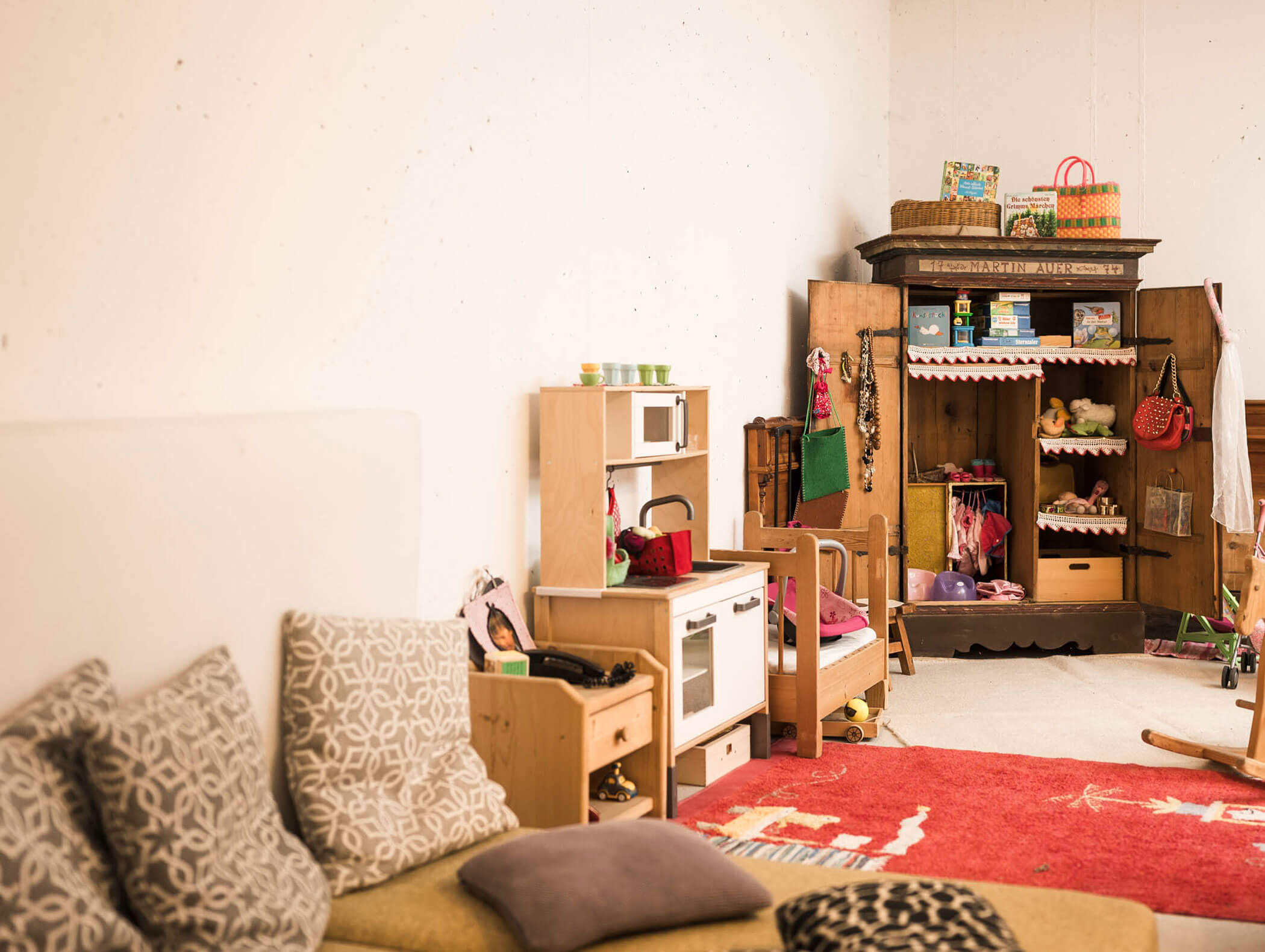 Gemütliches Spielzimmer mit Spielzeugküche, Kleiderschrank, Sofa, Kissen, rotem Teppich und verschiedenen Spielsachen. - Maurlechnhof