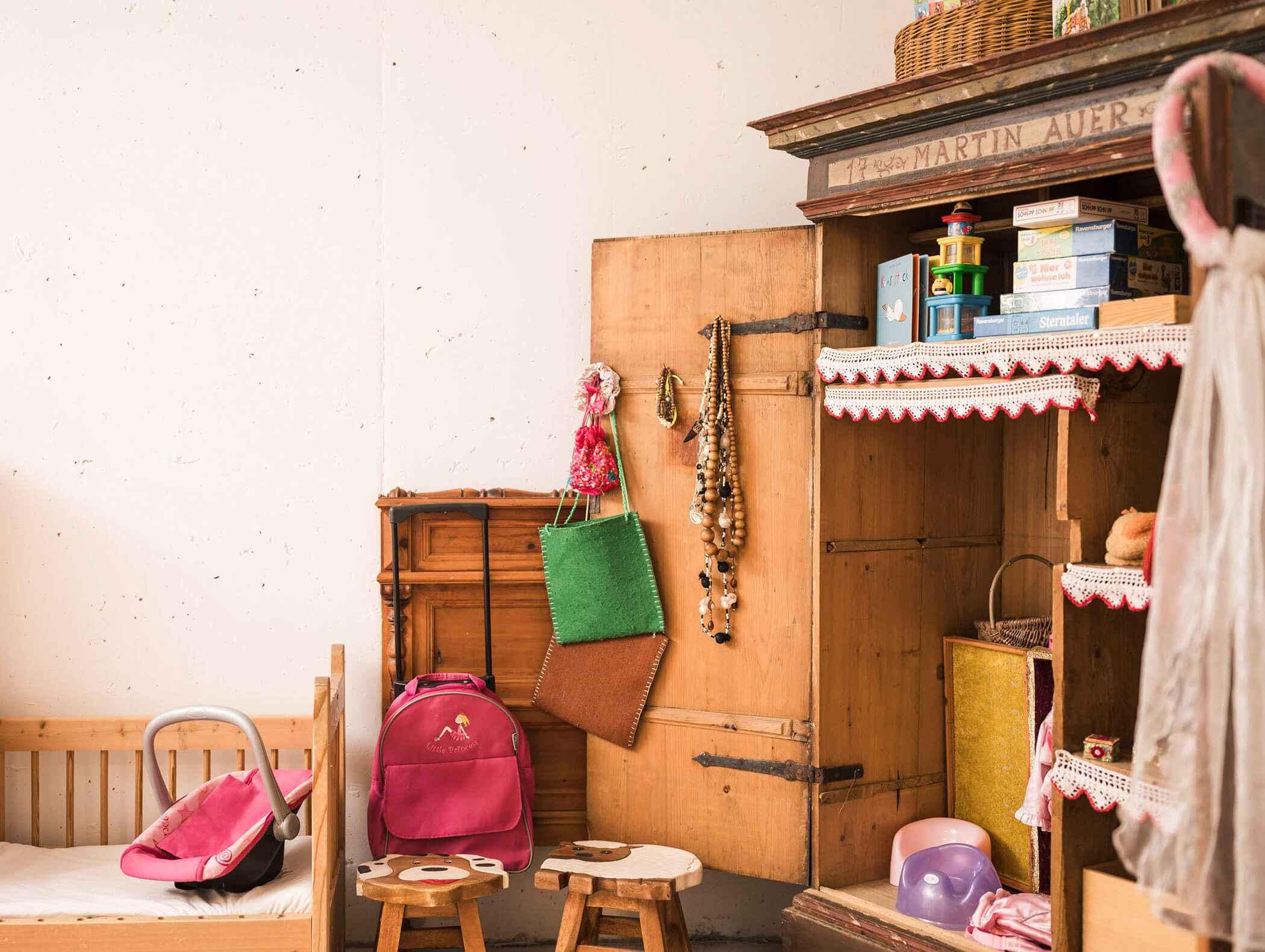 Gemütliches Kinderzimmer mit Kinderbett, rosa Rucksack, offenem Kleiderschrank, Spielzeug und bunten Taschen, die an der Tür hängen. - Maurlechnhof