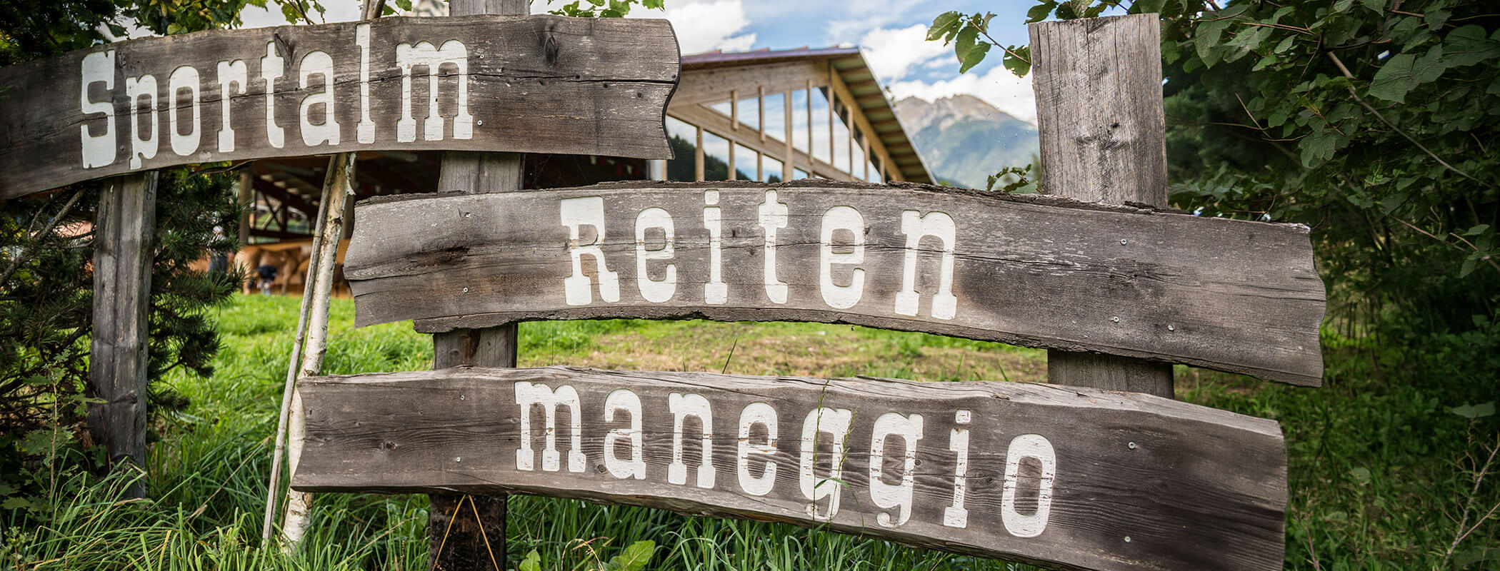 Three rustic wooden signs with the words Sportalm, Reiten, and Maneggio in white letters, outdoors. - Maurlechnhof