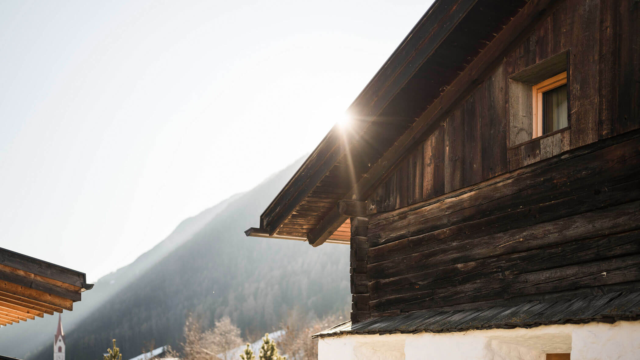 Das Sonnenlicht scheint durch das Dach einer rustikalen Holzhütte mit Bergen im Hintergrund. - Maurlechnhof