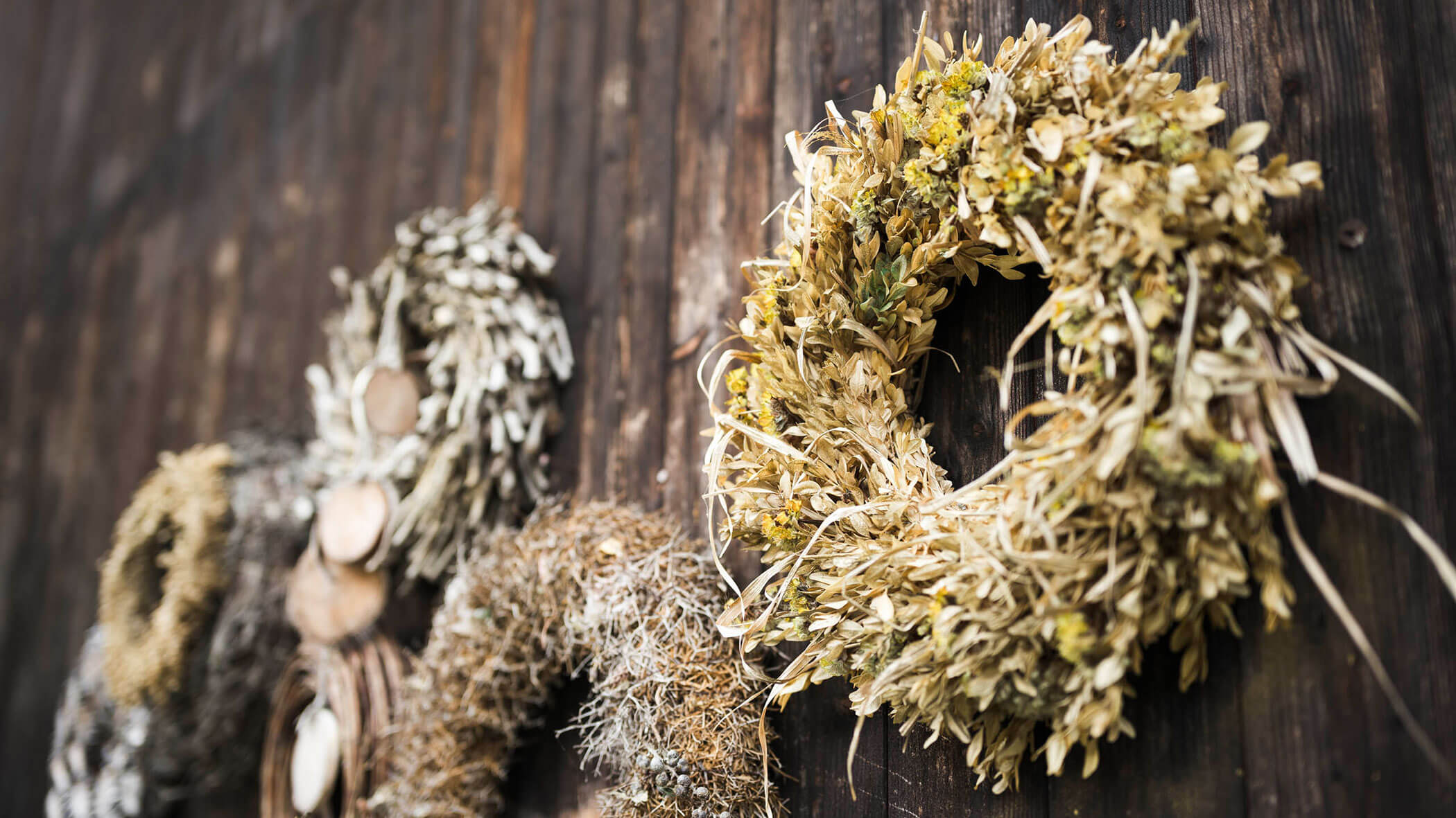 Getrocknete Blumenkränze hängen an einer rustikalen Wand aus dunklem Holz. - Maurlechnhof