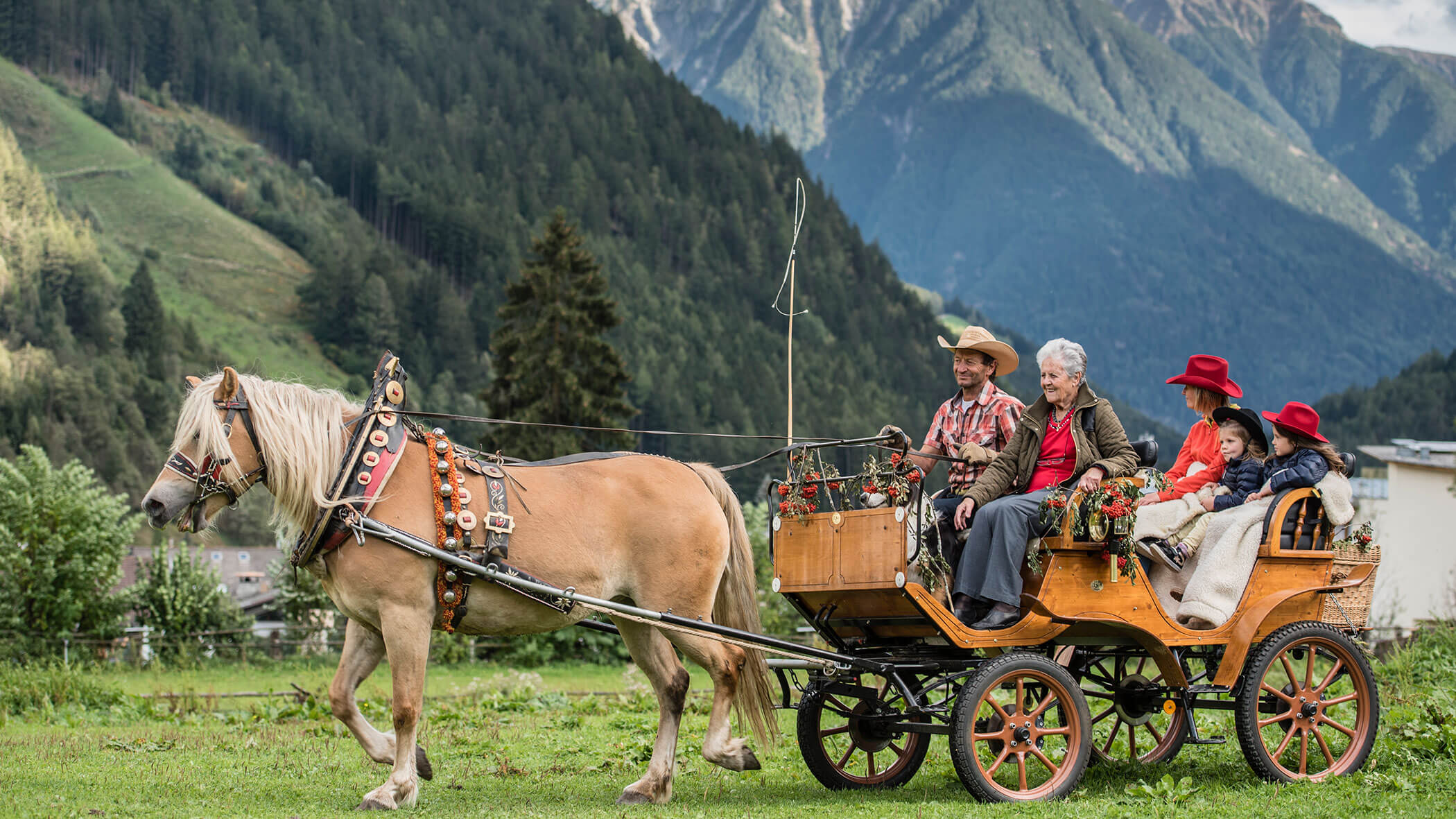 A horse pulls a wooden carriage with five people in hats, riding through a scenic mountain landscape. - Maurlechnhof