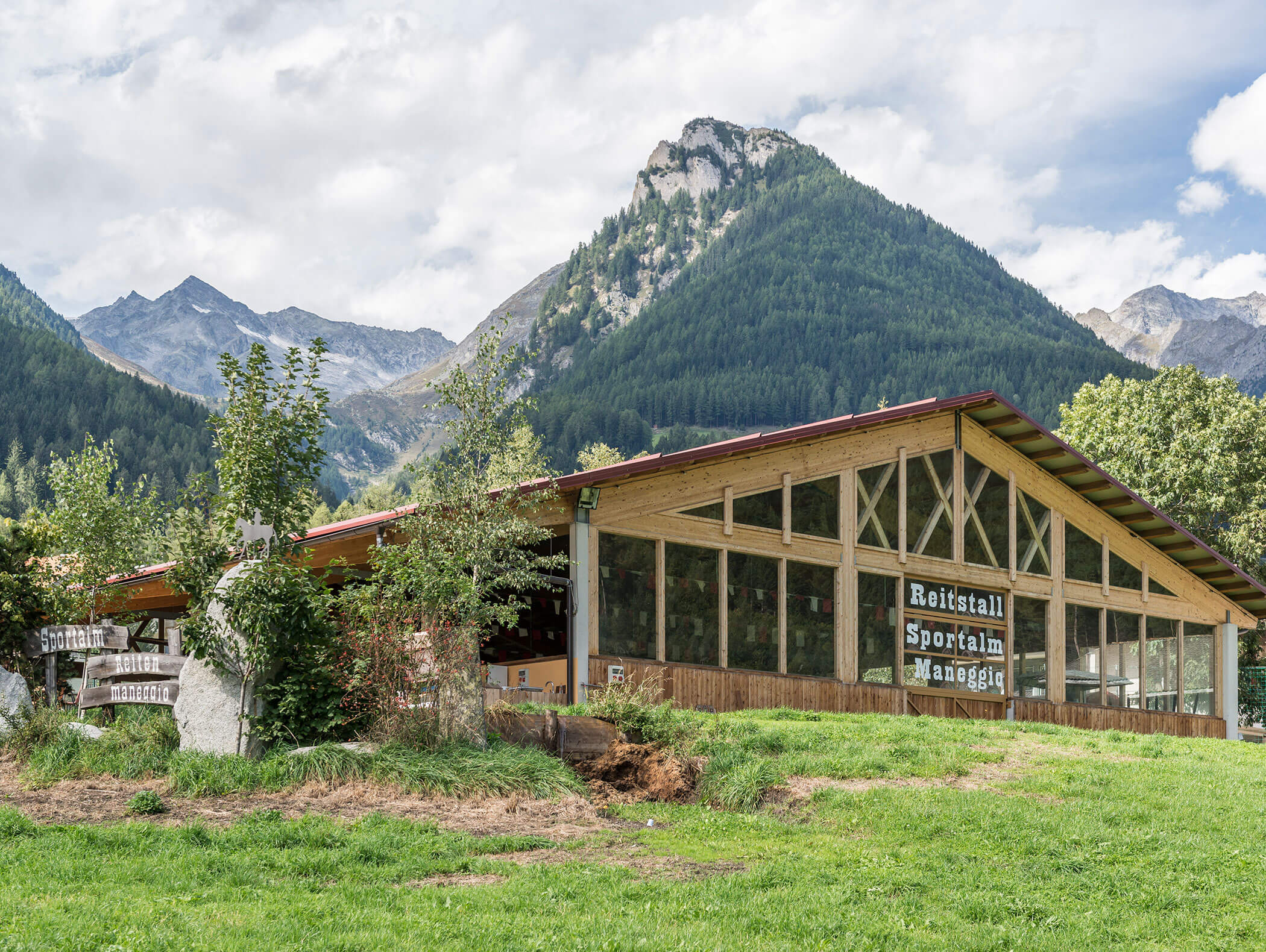 Holzgebäude mit großen Fenstern auf einer grünen Wiese, Berge und Bäume im Hintergrund. - Maurlechnhof