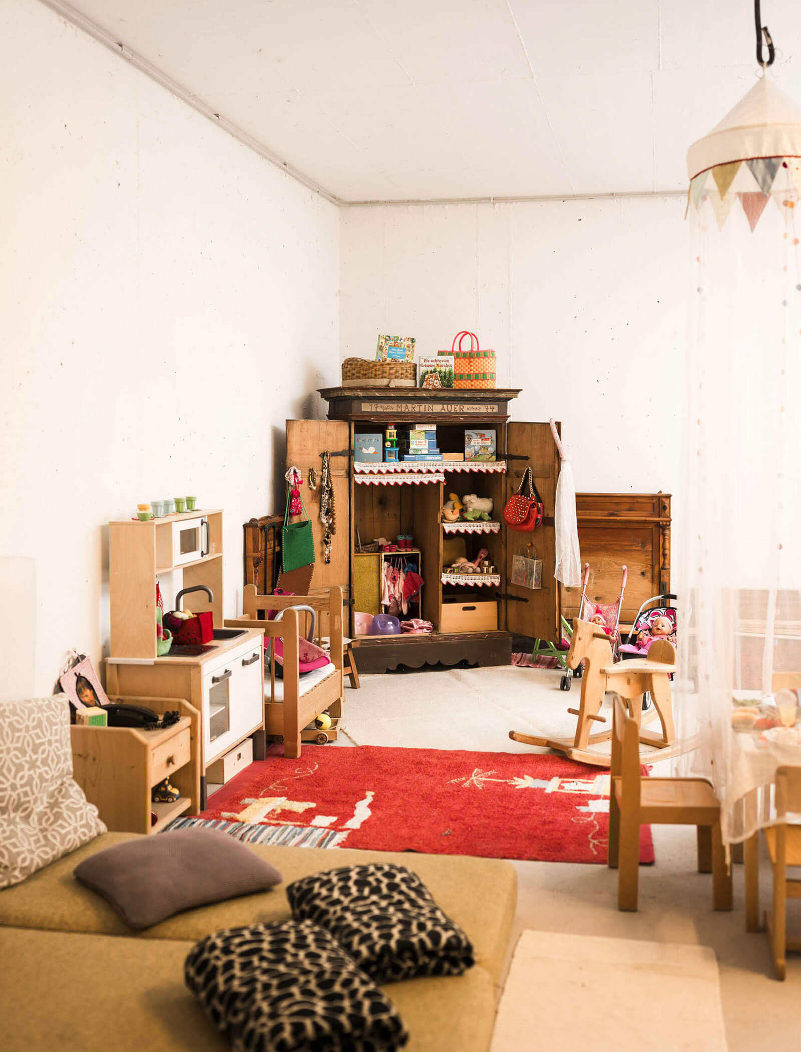 Ein gemütliches Spielzimmer mit Spielzeugküche, Holzschrank, Schaukelpferd, Sofa und rotem Teppich auf dem Boden. - Maurlechnhof