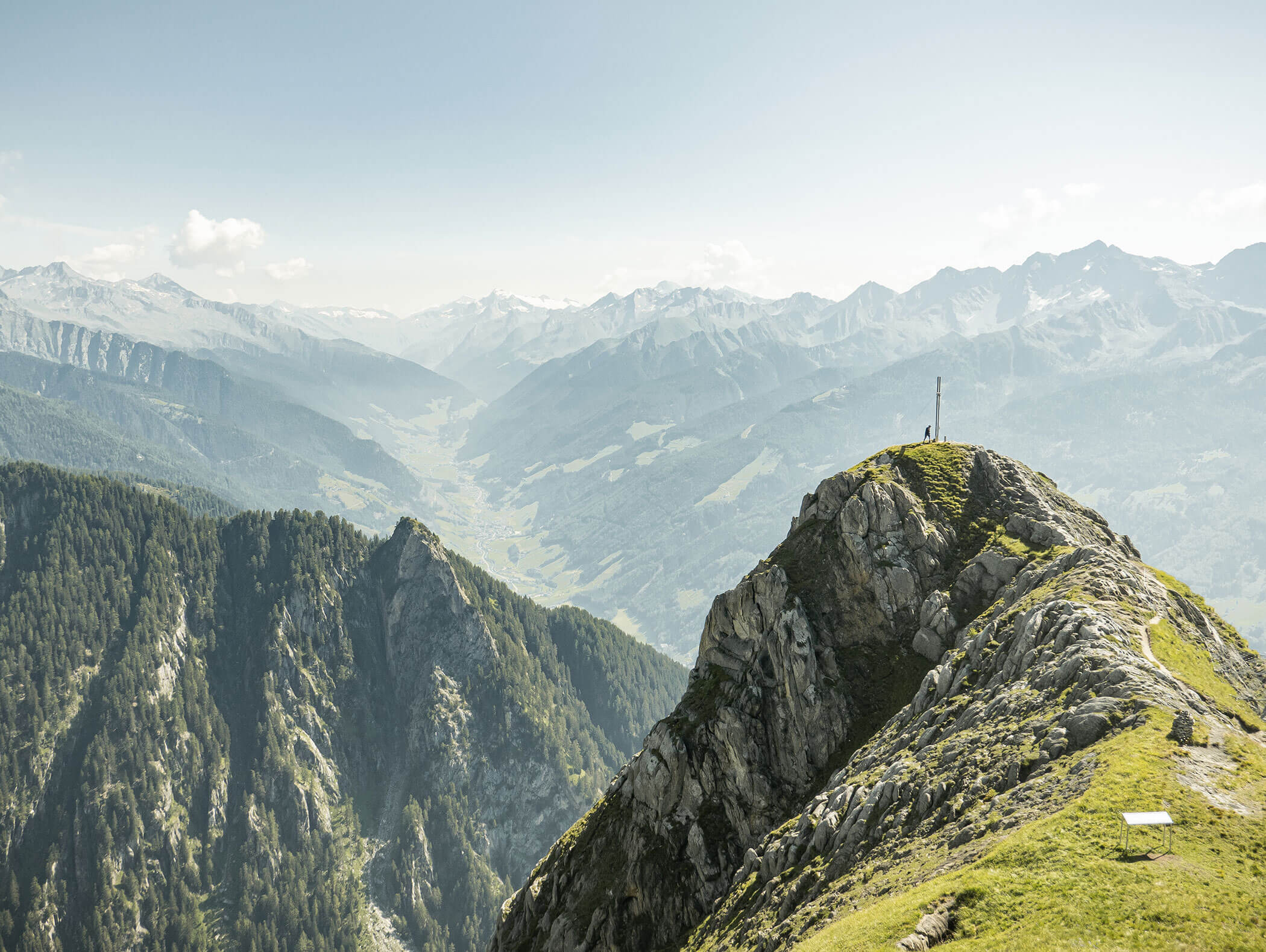 Mountain peak with a cross, overlooking a valley and distant mountain ranges under a clear sky. - Maurlechnhof