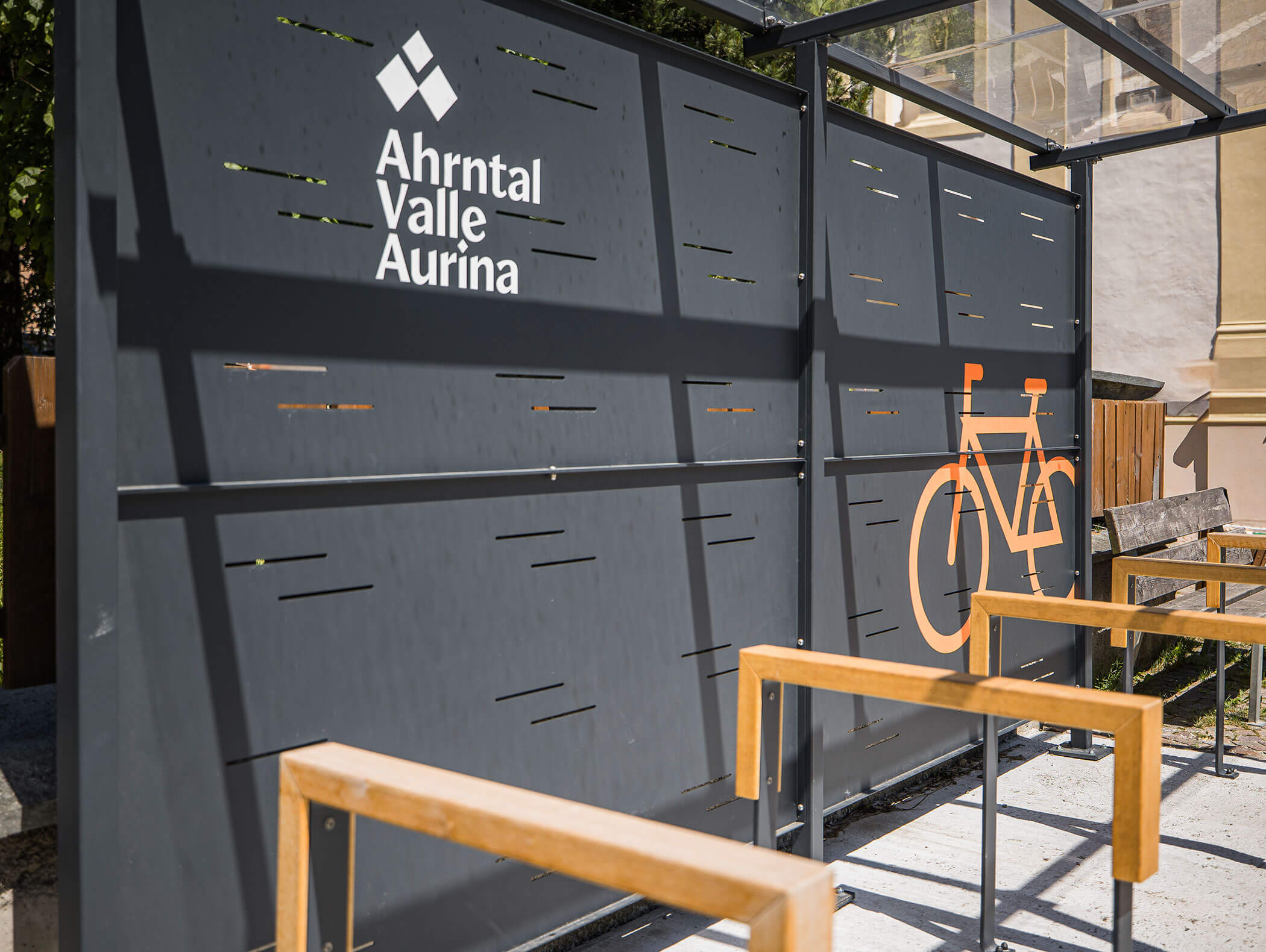 Bicycle parking area with Ahrntal Valle Aurina sign and an orange bike symbol on a metal wall. - Maurlechnhof