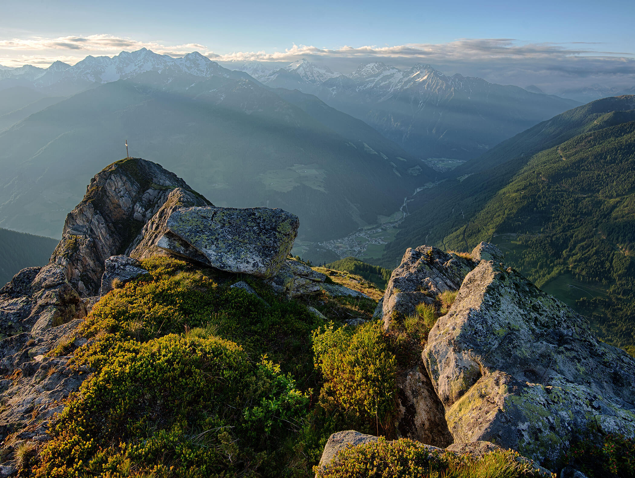 Rocky mountain peak with green moss, overlooking a valley and distant snow-capped mountains at sunrise. - Maurlechnhof