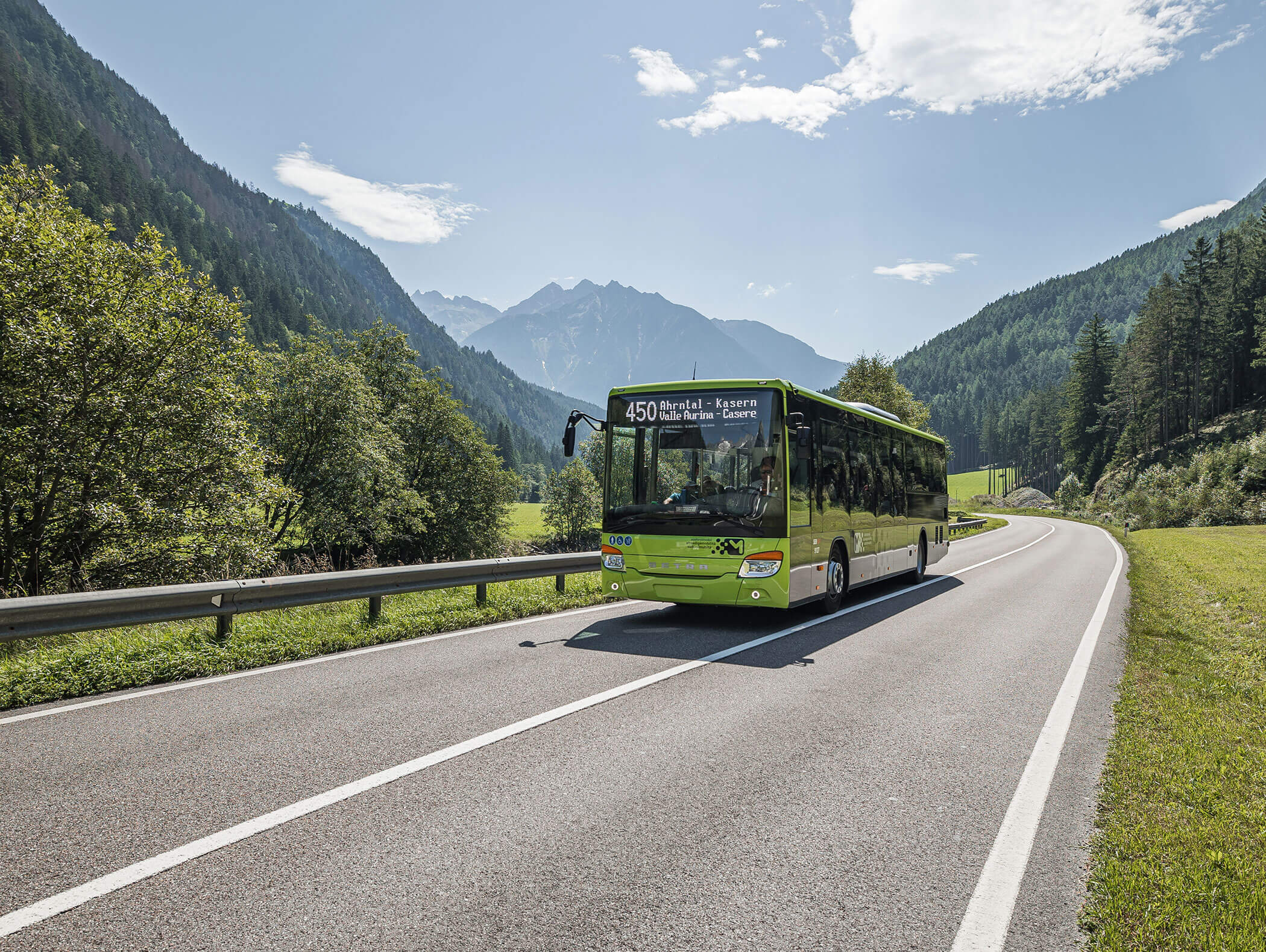 A green bus drives on a winding road through a scenic mountain landscape under a partly cloudy sky. - Maurlechnhof