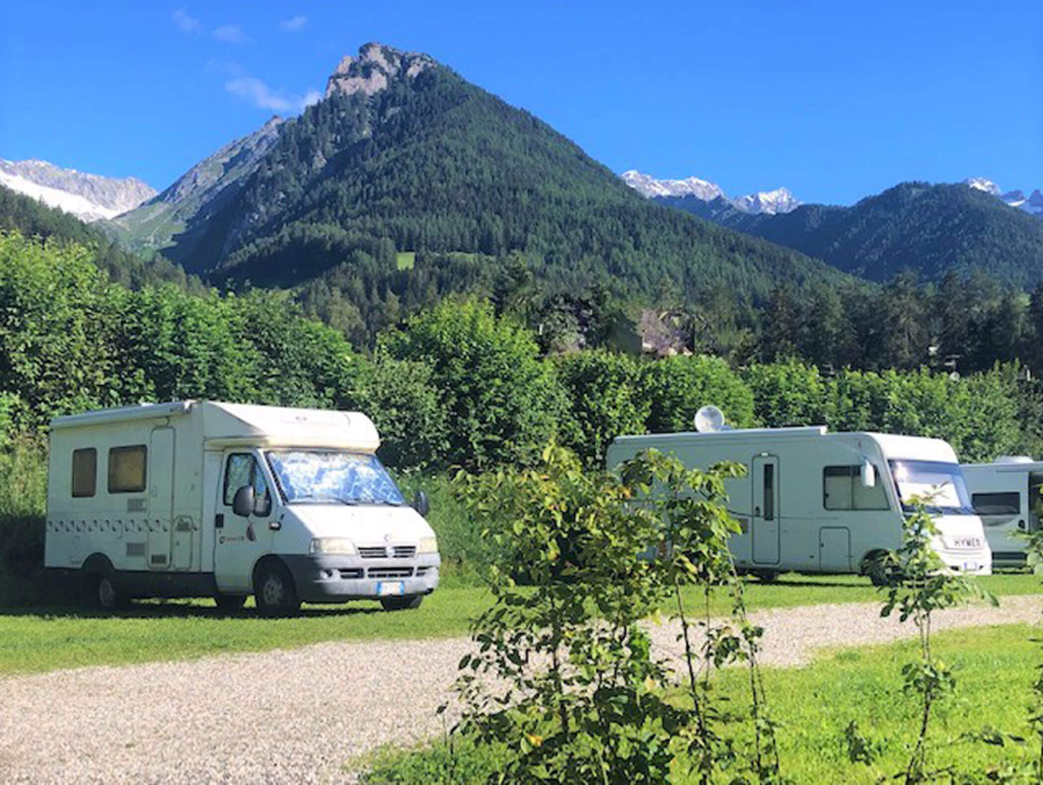 Zwei auf einer Wiese geparkte Wohnmobile mit grünen Bergen und blauem Himmel im Hintergrund. - Maurlechnhof