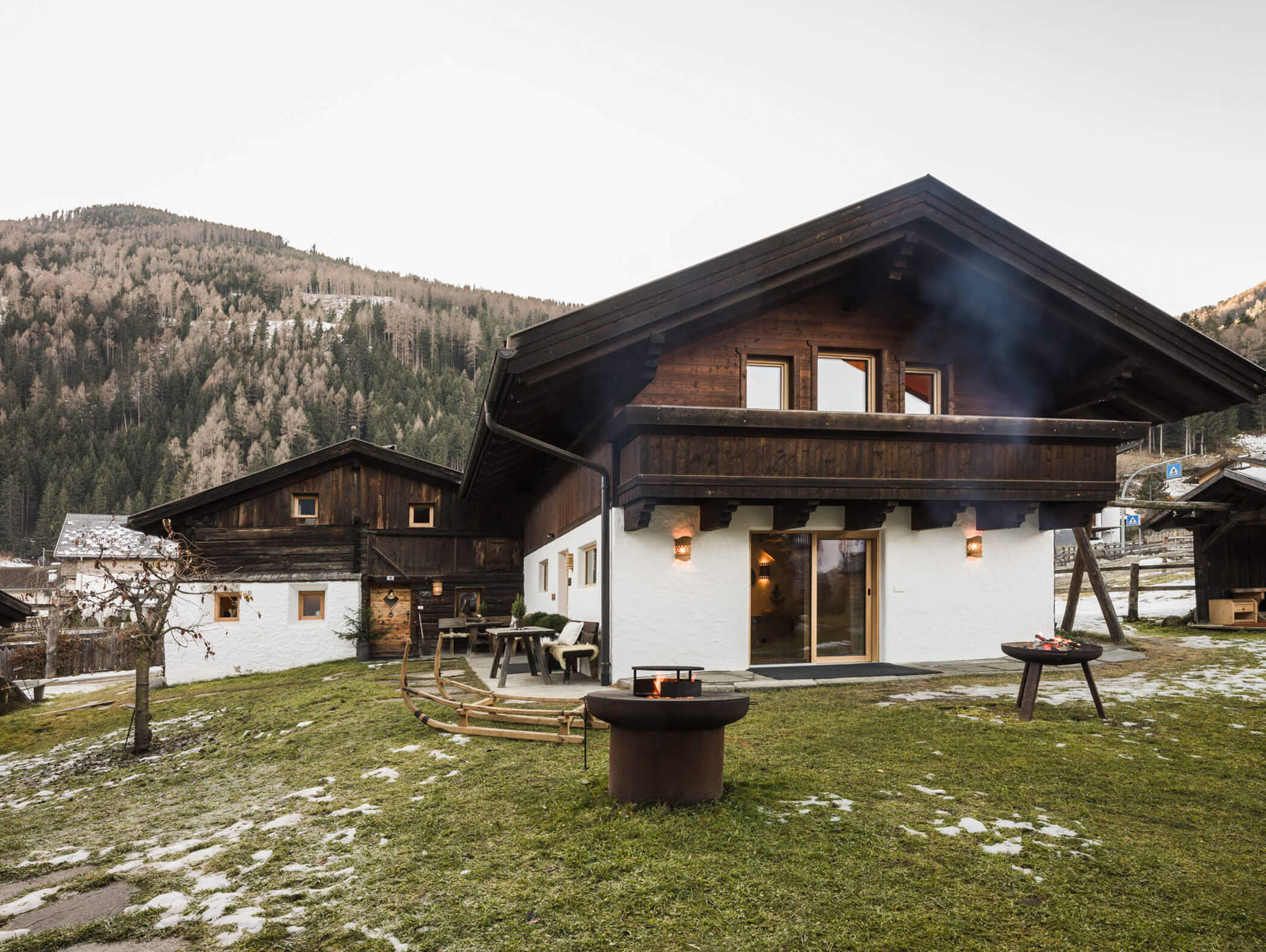 Eine gemütliche Holzhütte mit verschneitem Hof, Feuerstelle und Grill, eingebettet in eine Berglandschaft. - Maurlechnhof