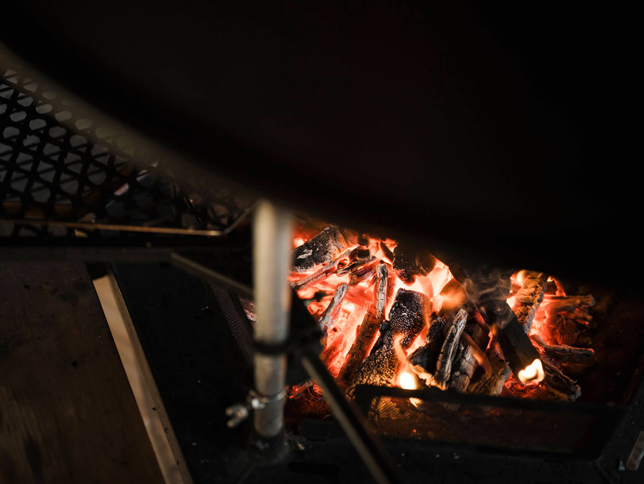 Brennende Holzscheite und glühende Glut in einem Metallkamin mit einem Grillrost darüber. - Maurlechnhof