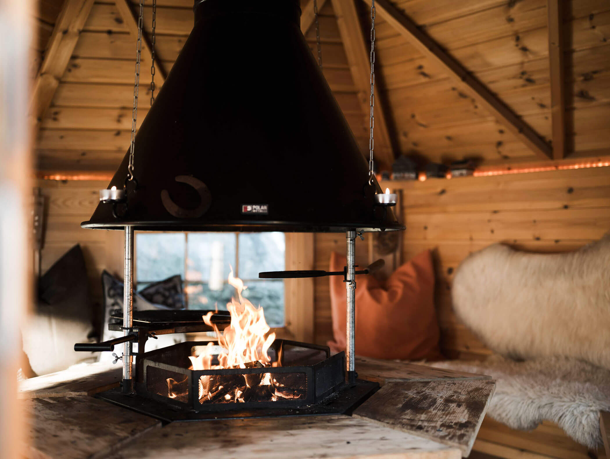 Eine gemütliche Holzhütte mit zentraler Feuerstelle, Bänken, Kissen und einer Schaffelldecke. - Maurlechnhof