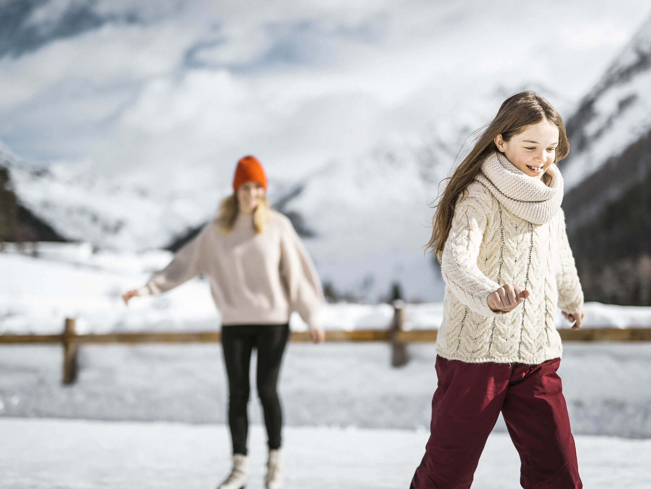 Zwei Personen, die an einem verschneiten Tag im Freien Schlittschuh laufen, mit Bergen im Hintergrund. - Maurlechnhof