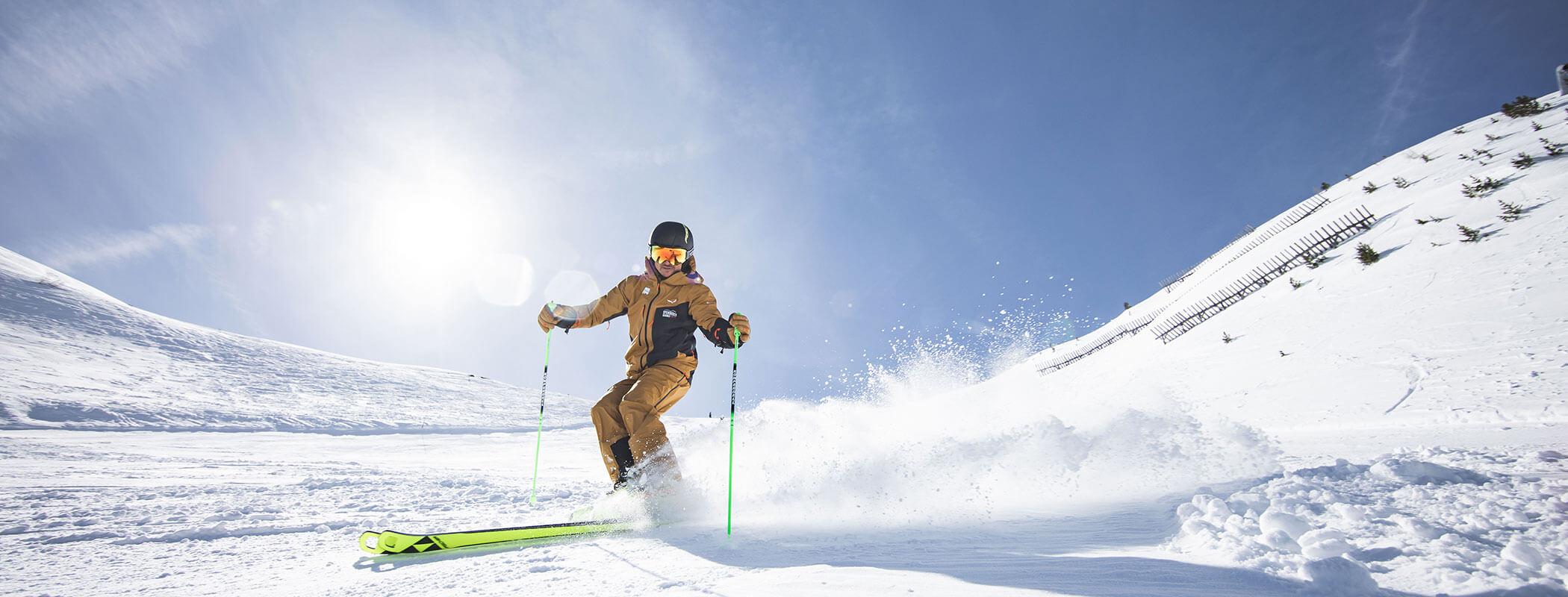 Ein Skifahrer in braunen Klamotten gleitet bei strahlend blauem Himmel und hellem Sonnenlicht einen verschneiten Hang hinunter. - Maurlechnhof